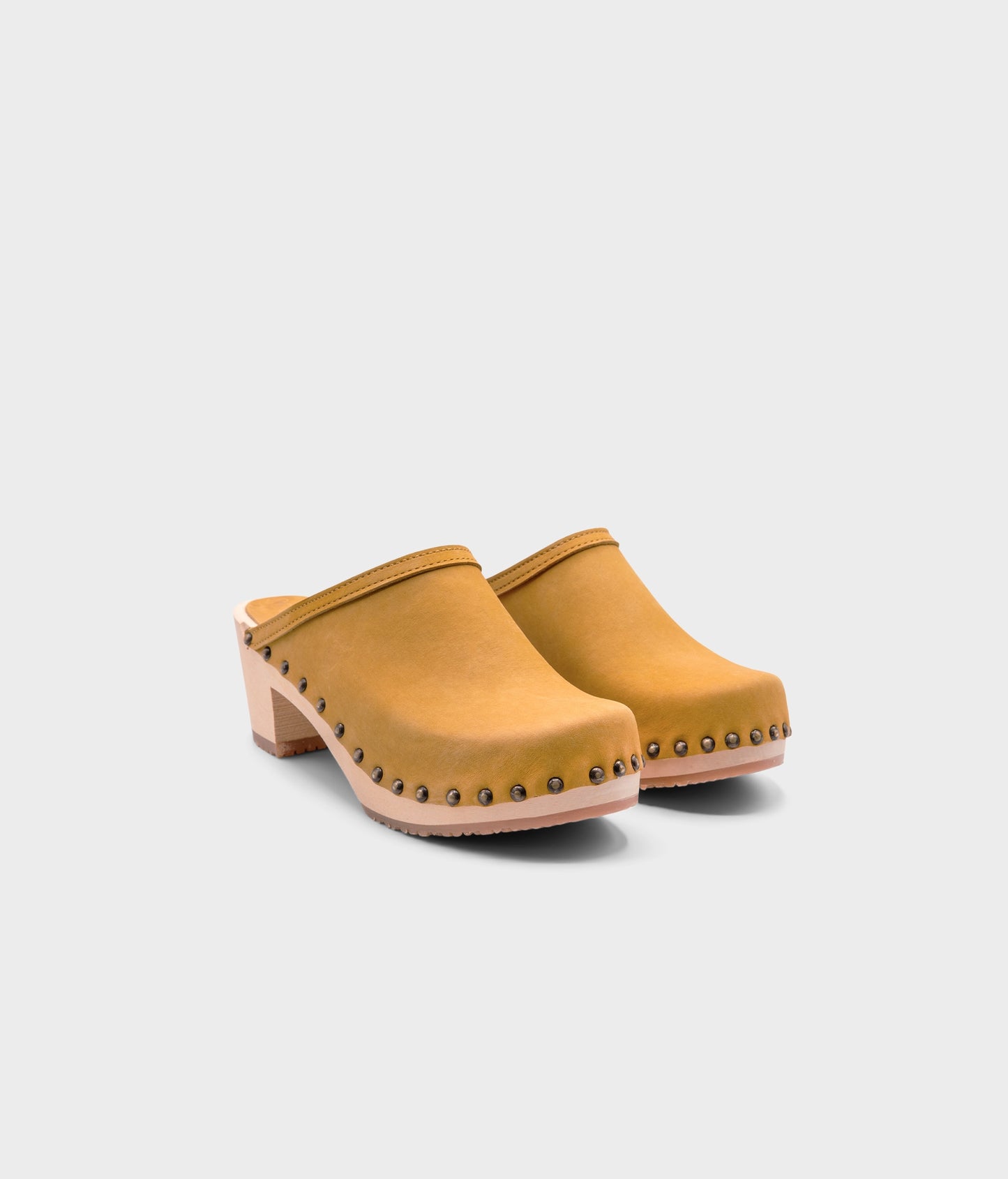 high heeled clog mules in yellow nubuck leather stapled on a light wooden base with brass gold studs