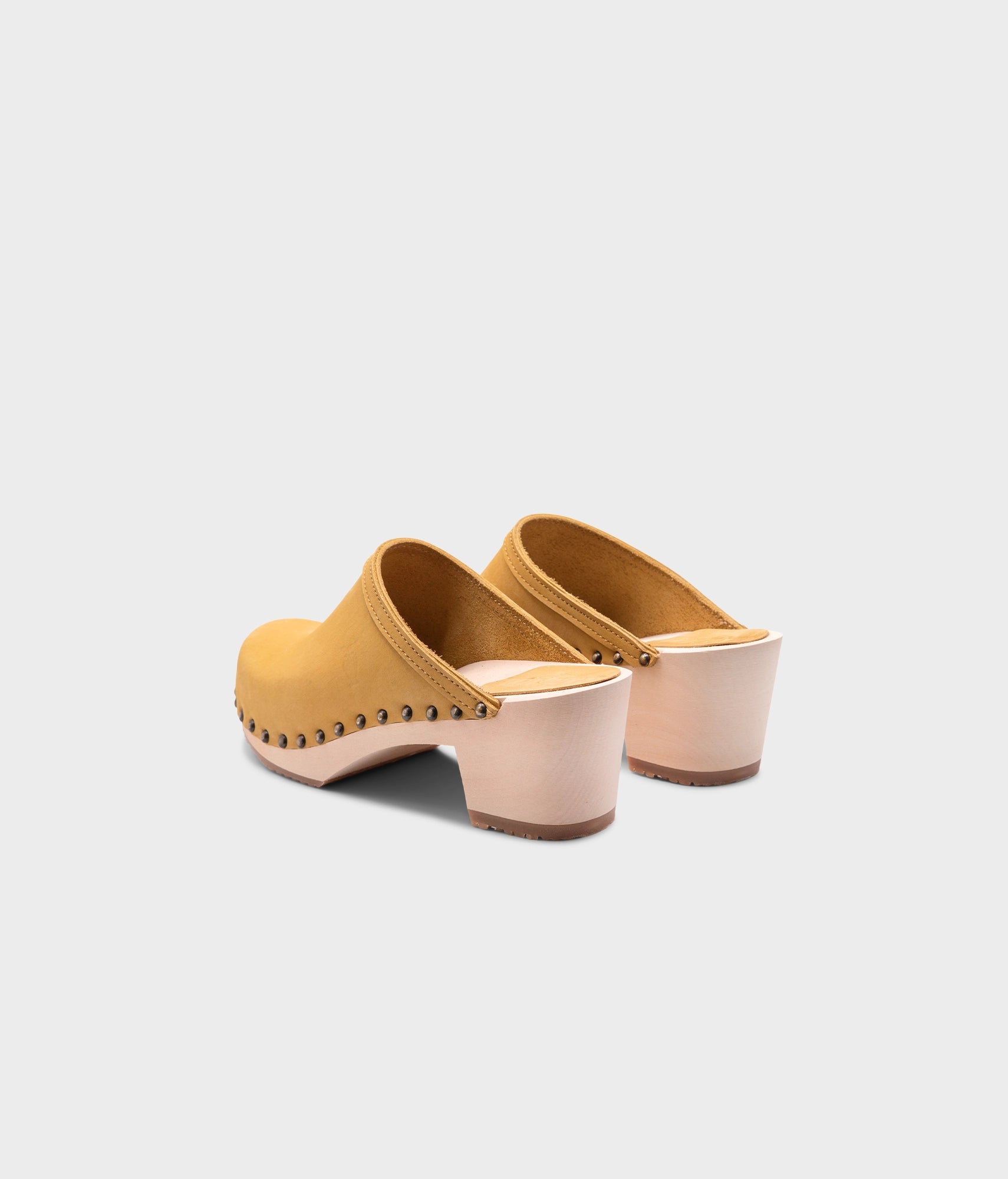 high heeled clog mules in yellow nubuck leather stapled on a light wooden base with brass gold studs