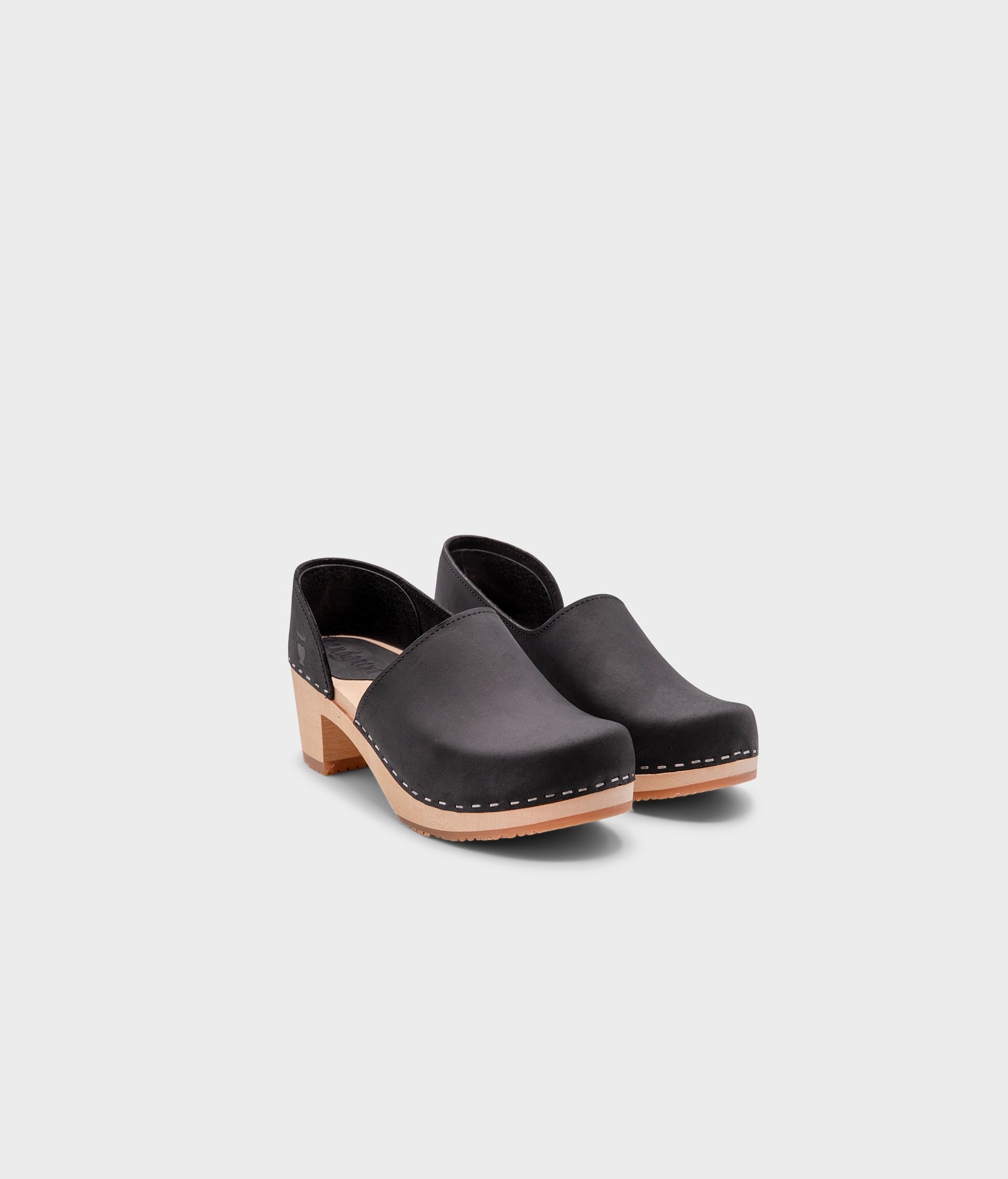 high heeled closed-back clogs in black nubuck leather stapled on a light wooden base