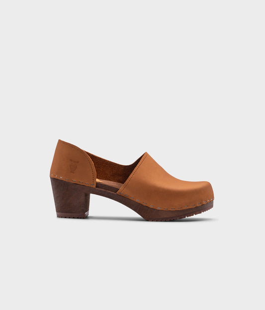 high heeled closed-back clogs in light brown nubuck leather stapled on a dark wooden base