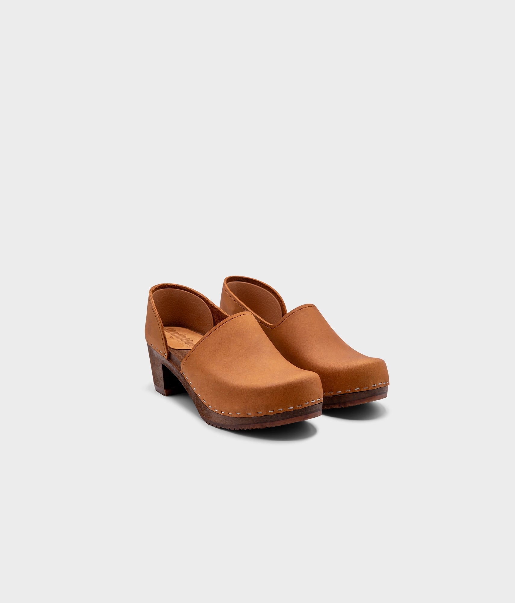 high heeled closed-back clogs in light brown nubuck leather stapled on a dark wooden base