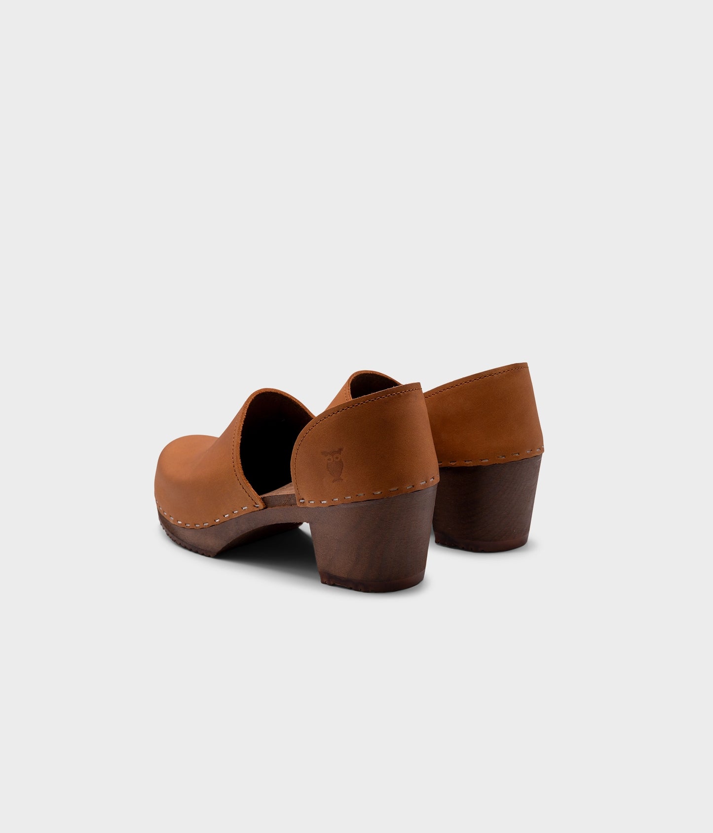 high heeled closed-back clogs in light brown nubuck leather stapled on a dark wooden base