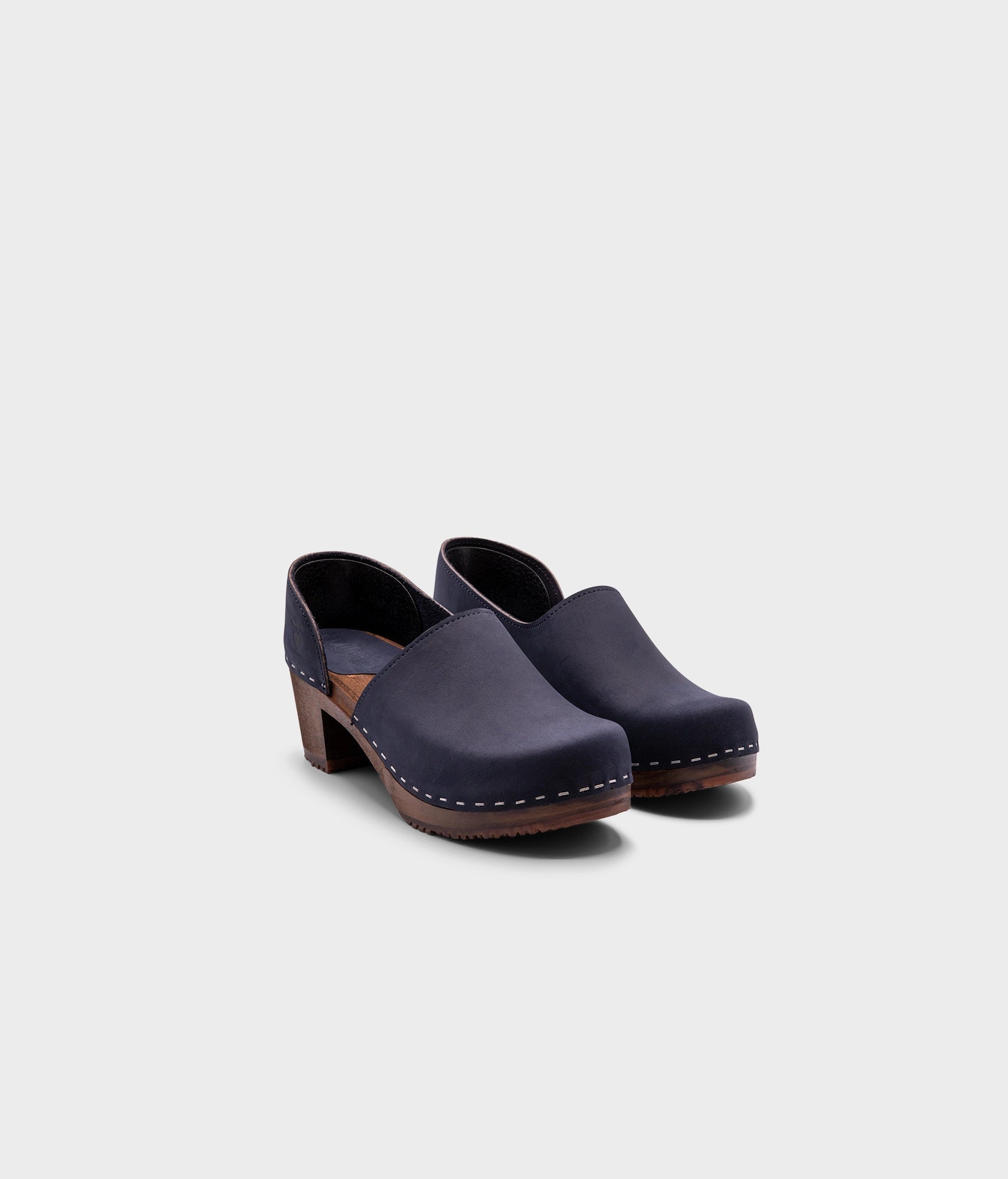 high heeled closed-back clogs in navy blue nubuck leather stapled on a dark wooden base