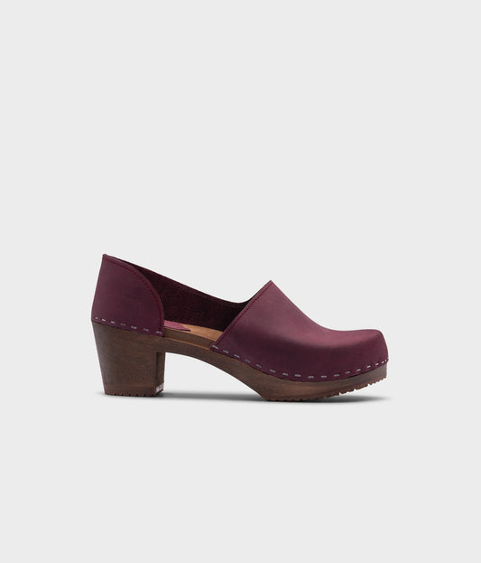 high heeled closed-back clogs in purple plum nubuck leather stapled on a dark wooden base