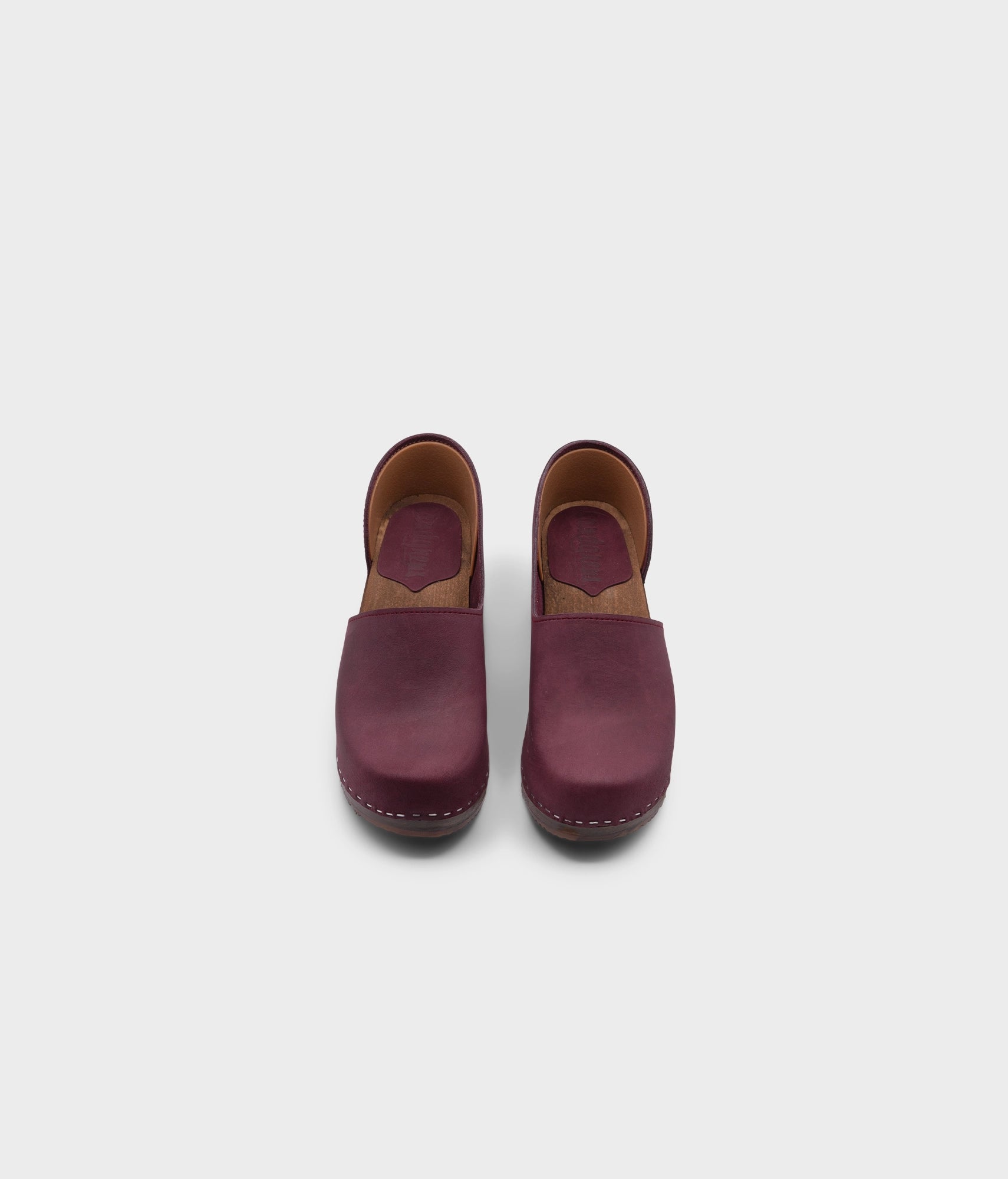 high heeled closed-back clogs in purple plum nubuck leather stapled on a dark wooden base