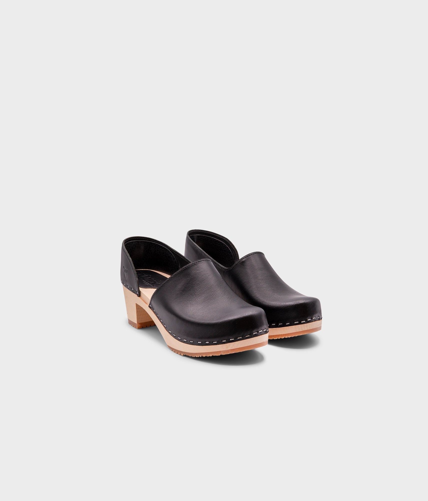 high heeled closed-back clogs in black vegetable tanned leather stapled on a light wooden base