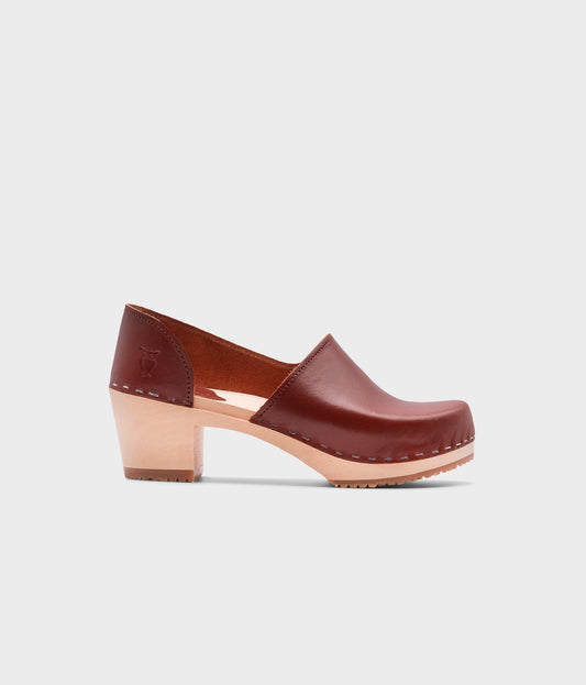 high heeled closed-back clogs in red cognac vegetable tanned leather stapled on a light wooden base