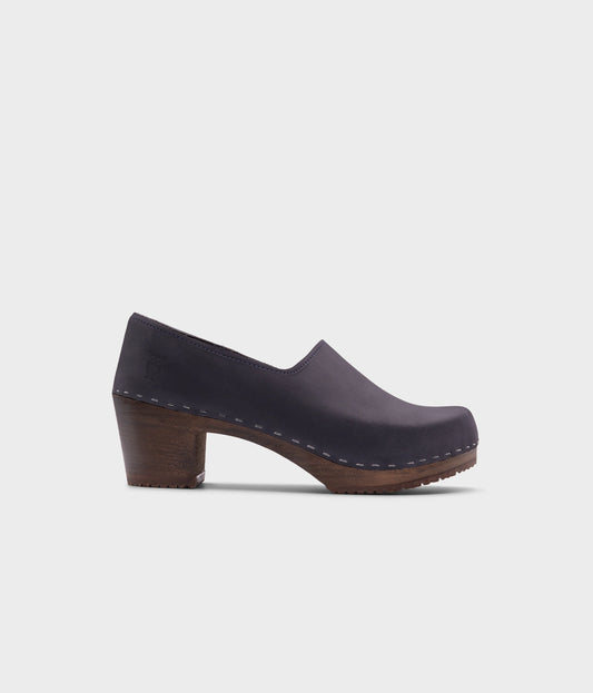 high heeled closed-back clogs in navy blue nubuck leather stapled on a dark wooden base