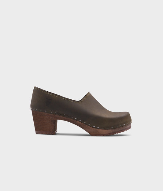 high heeled closed-back clogs in olive green nubuck leather stapled on a dark wooden base
