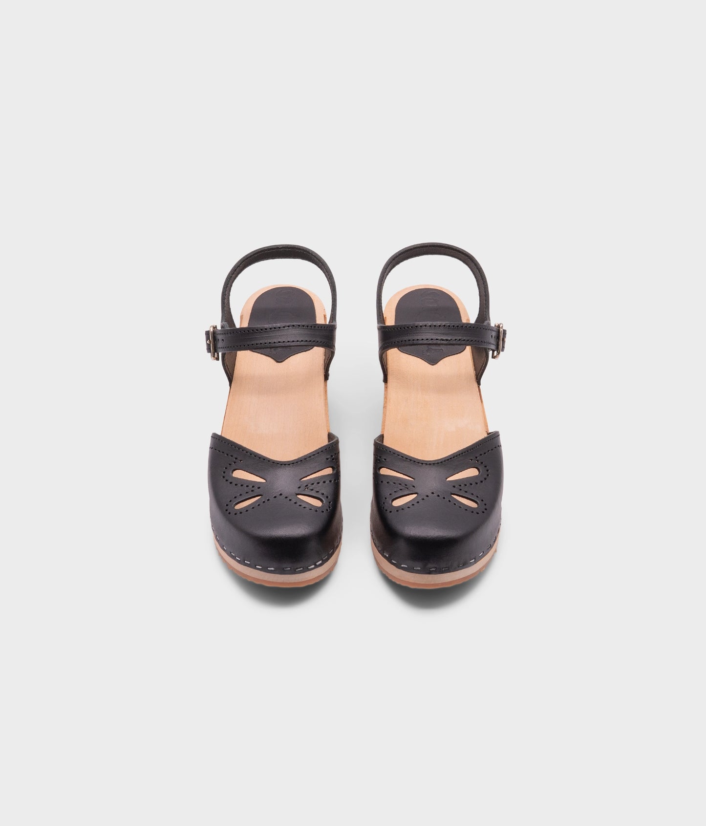 high-heeled clog sandal in black vegetable tanned leather with a blossom cut-out over the toe stapled on a light wooden base