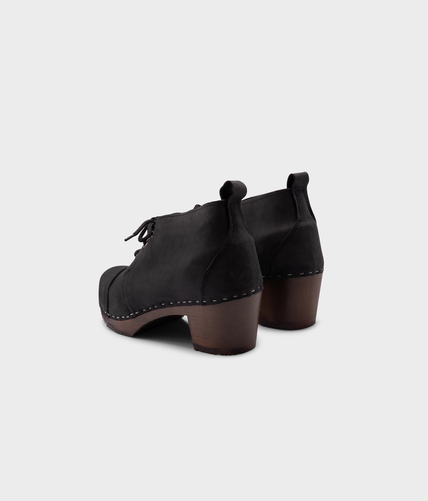 high heeled chukka clog boots in black nubuck leather stapled on a dark wooden base with black laces