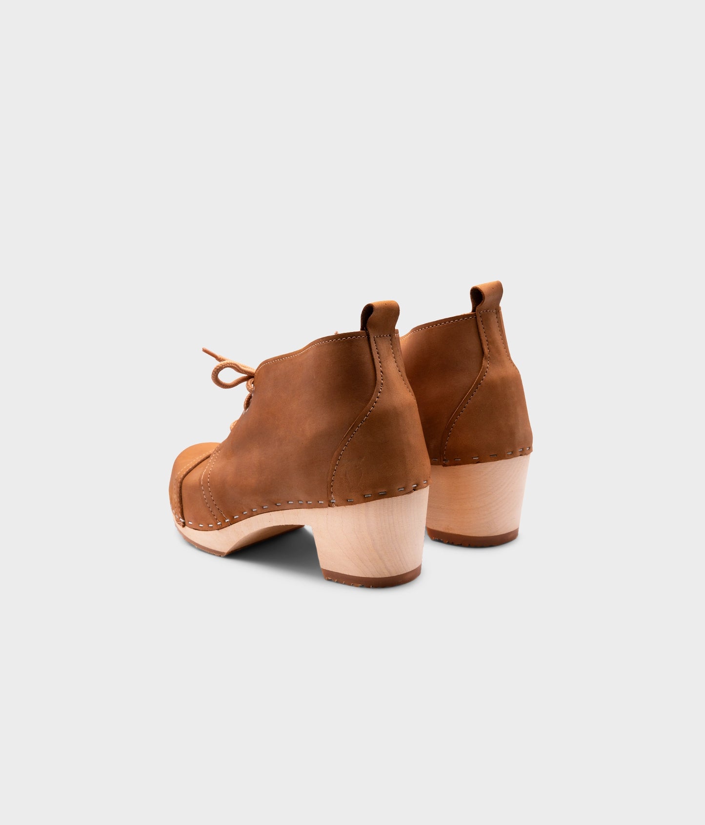 high heeled chukka clog boots in light brown nubuck leather stapled on a light wooden base with beige laces