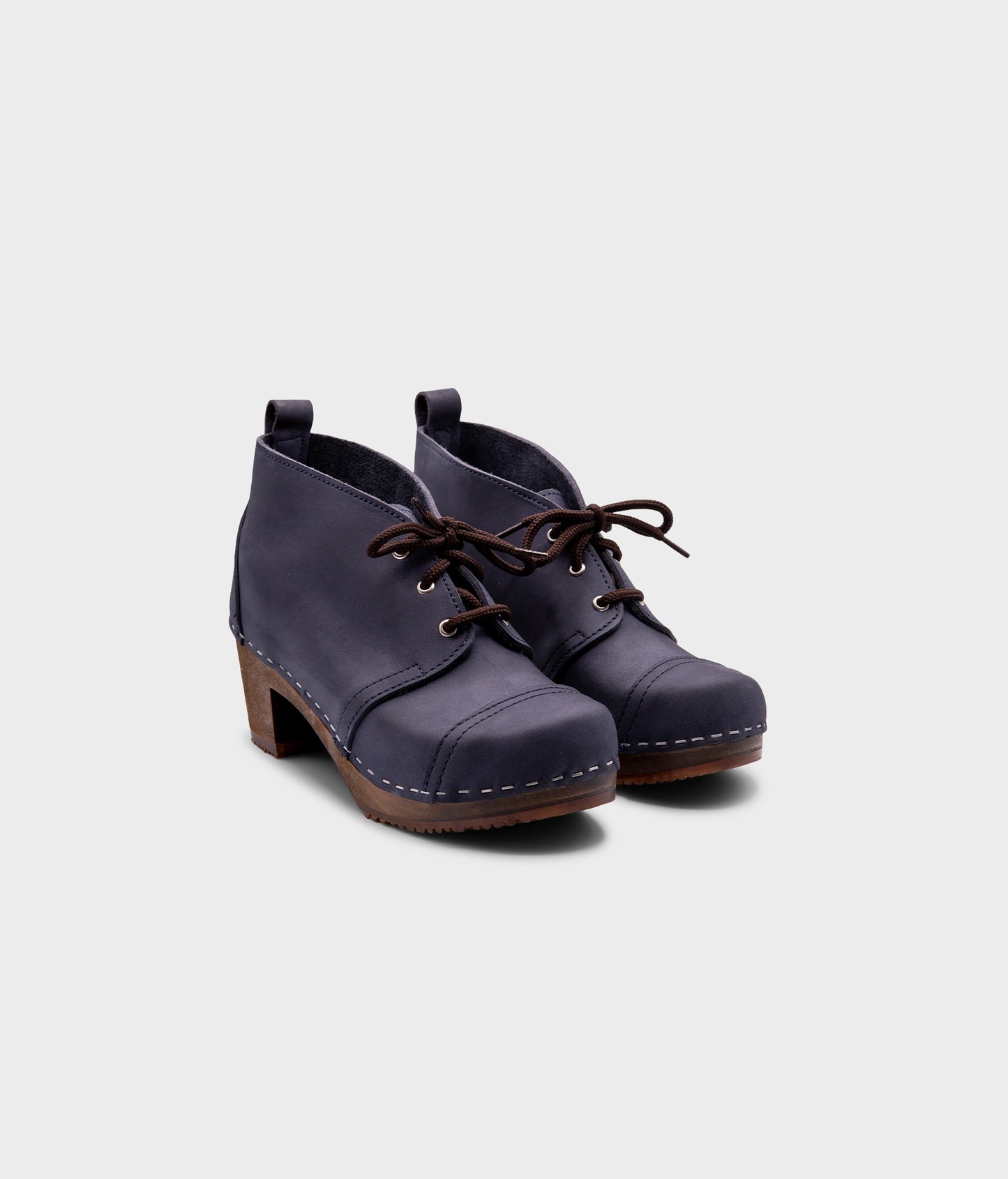 high heeled chukka clog boots in navy blue nubuck leather stapled on a dark wooden base with brown laces