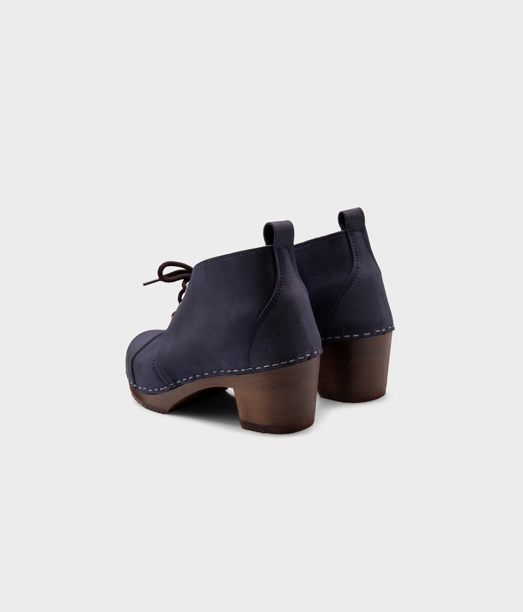 high heeled chukka clog boots in navy blue nubuck leather stapled on a dark wooden base with brown laces