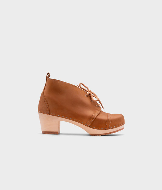 high heeled chukka clog boots in light brown nubuck leather stapled on a light wooden base with beige laces