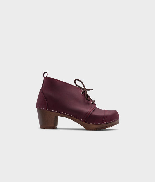 high heeled chukka clog boots in purple plum nubuck leather stapled on a dark wooden base with brown laces