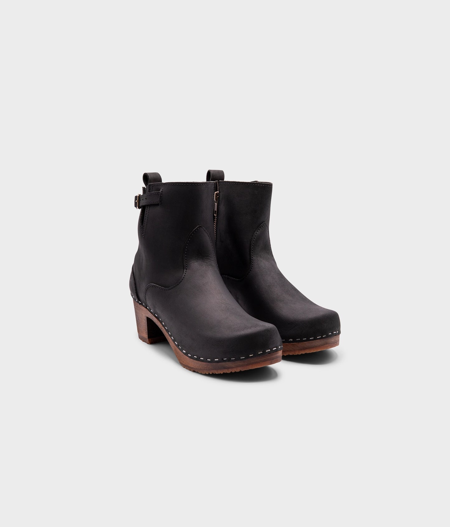 high-heeled clog boots in black nubuck leather stapled on a dark wooden base with a silver buckle