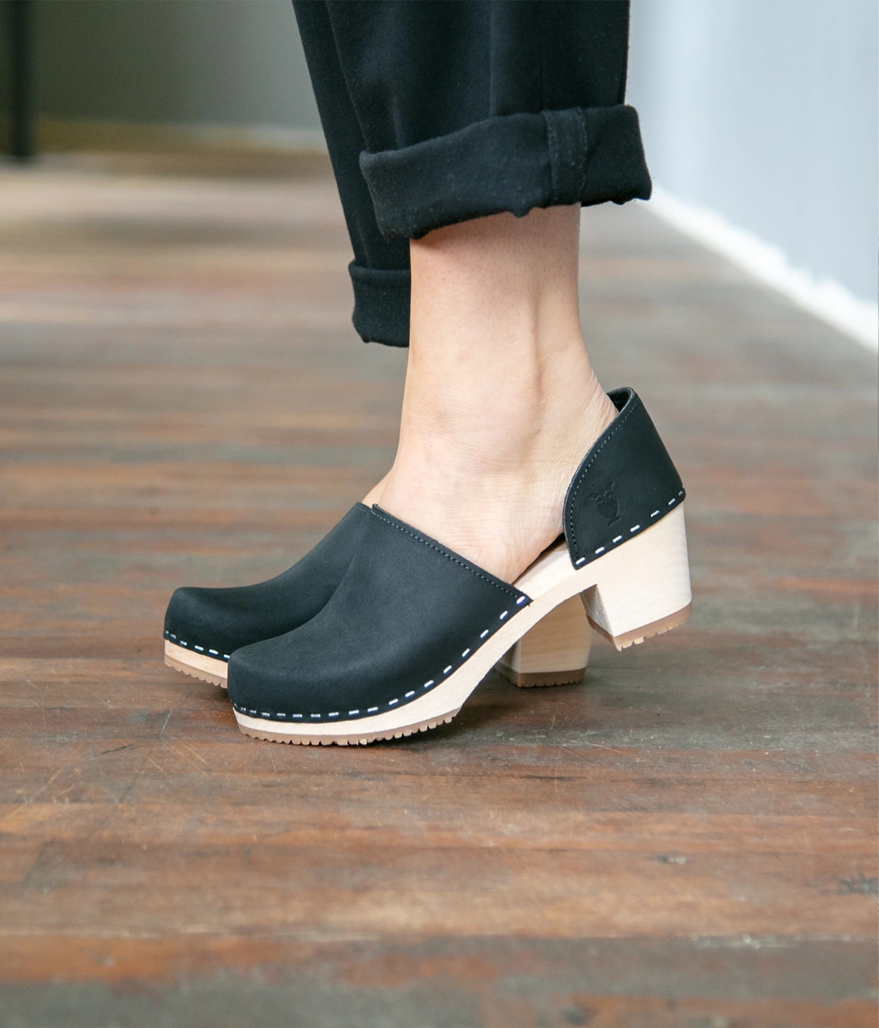 high heeled closed-back clogs in black nubuck leather stapled on a light wooden base