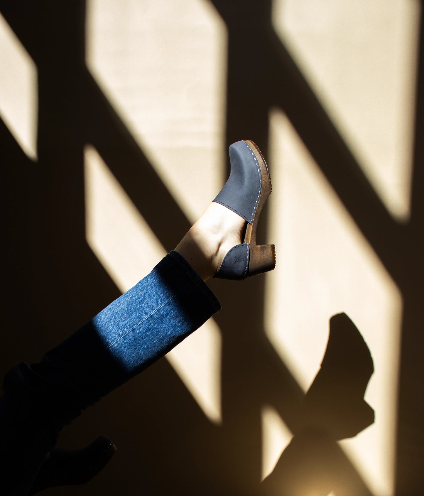 high heeled closed-back clogs in navy blue nubuck leather stapled on a dark wooden base