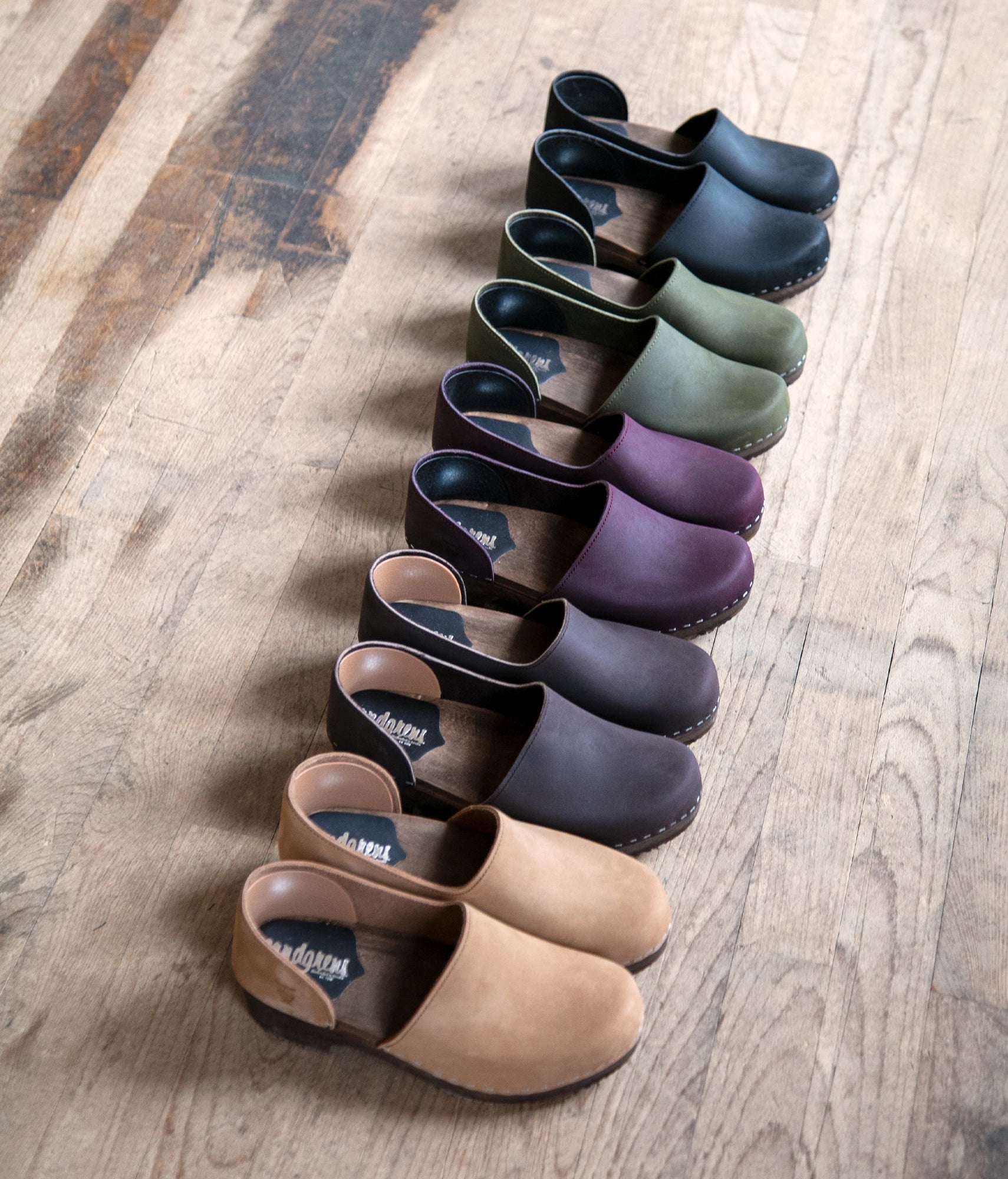 low heeled closed-back clogs in olive green nubuck leather stapled on a dark wooden base