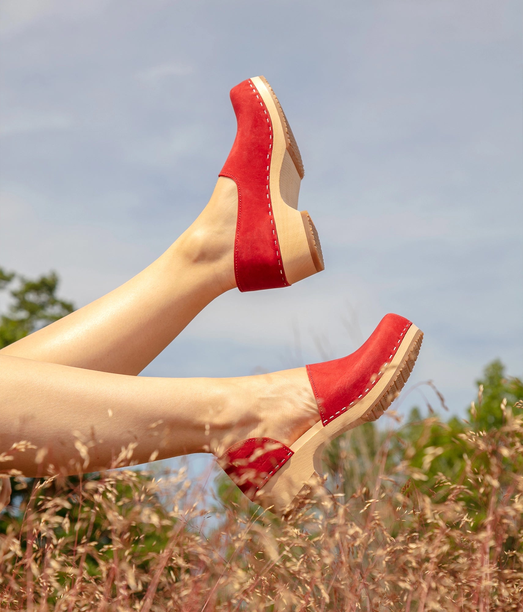 low heeled closed-back clogs in red nubuck leather stapled on a light wooden base