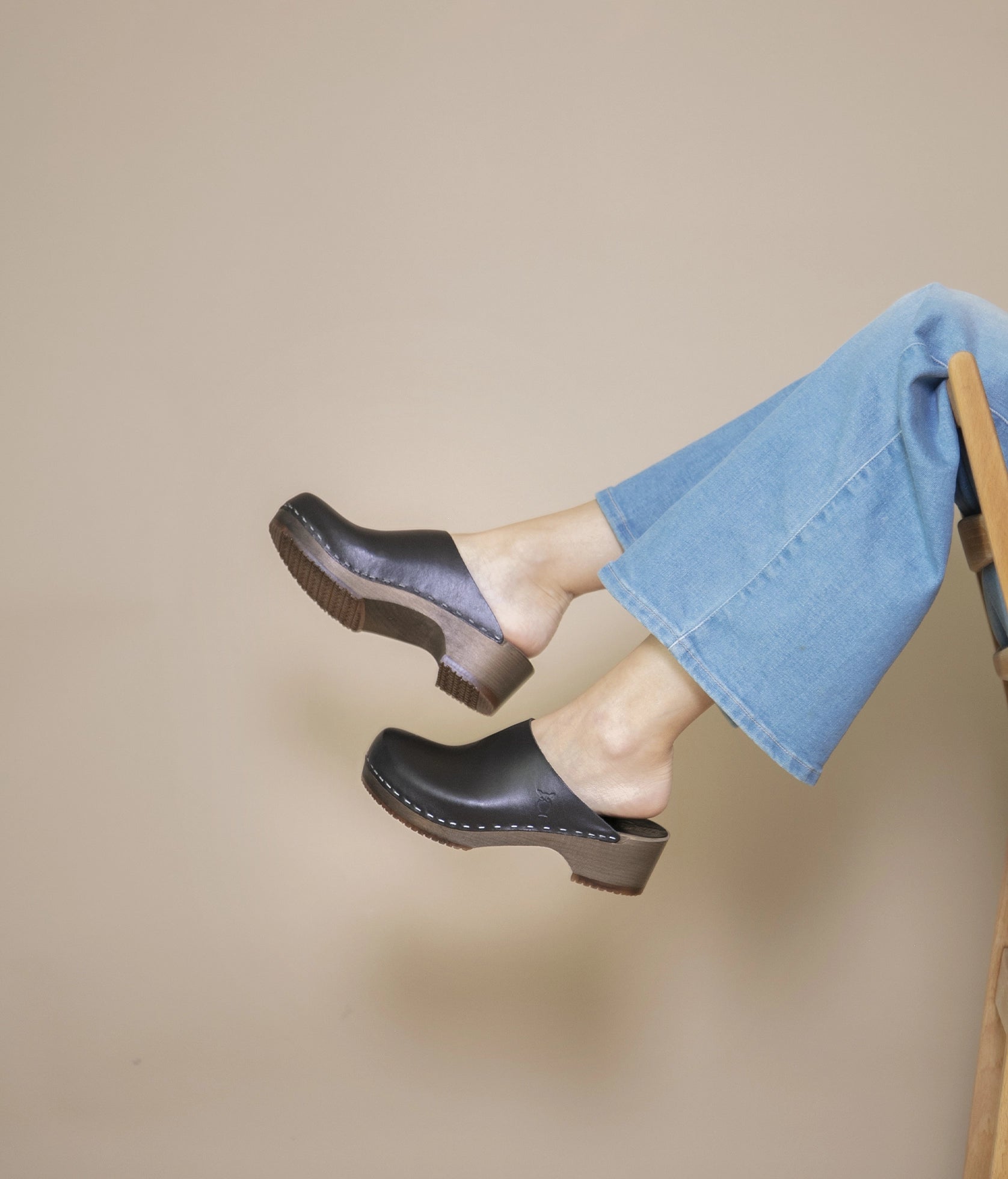 low heeled minimalistic clog mules in black vegetable tanned leather stapled on a dark wooden base