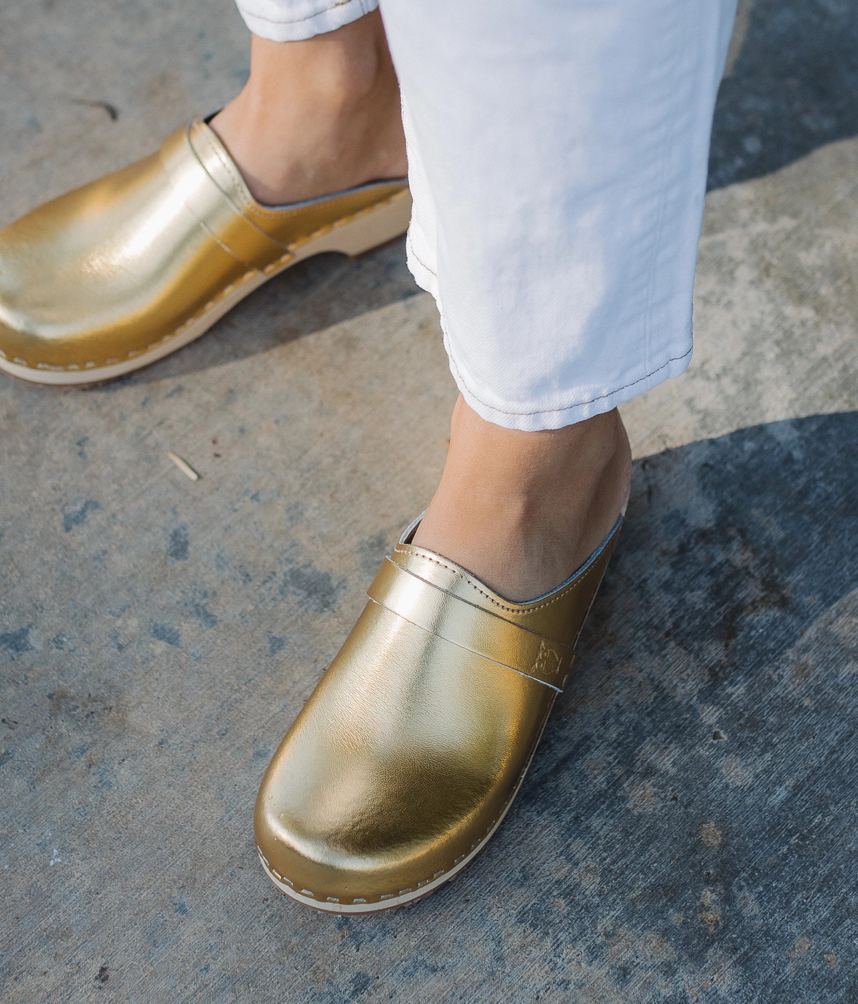 classic low heeled clog mule in metallic gold traditional leather stapled on a light wooden base with a leather strap