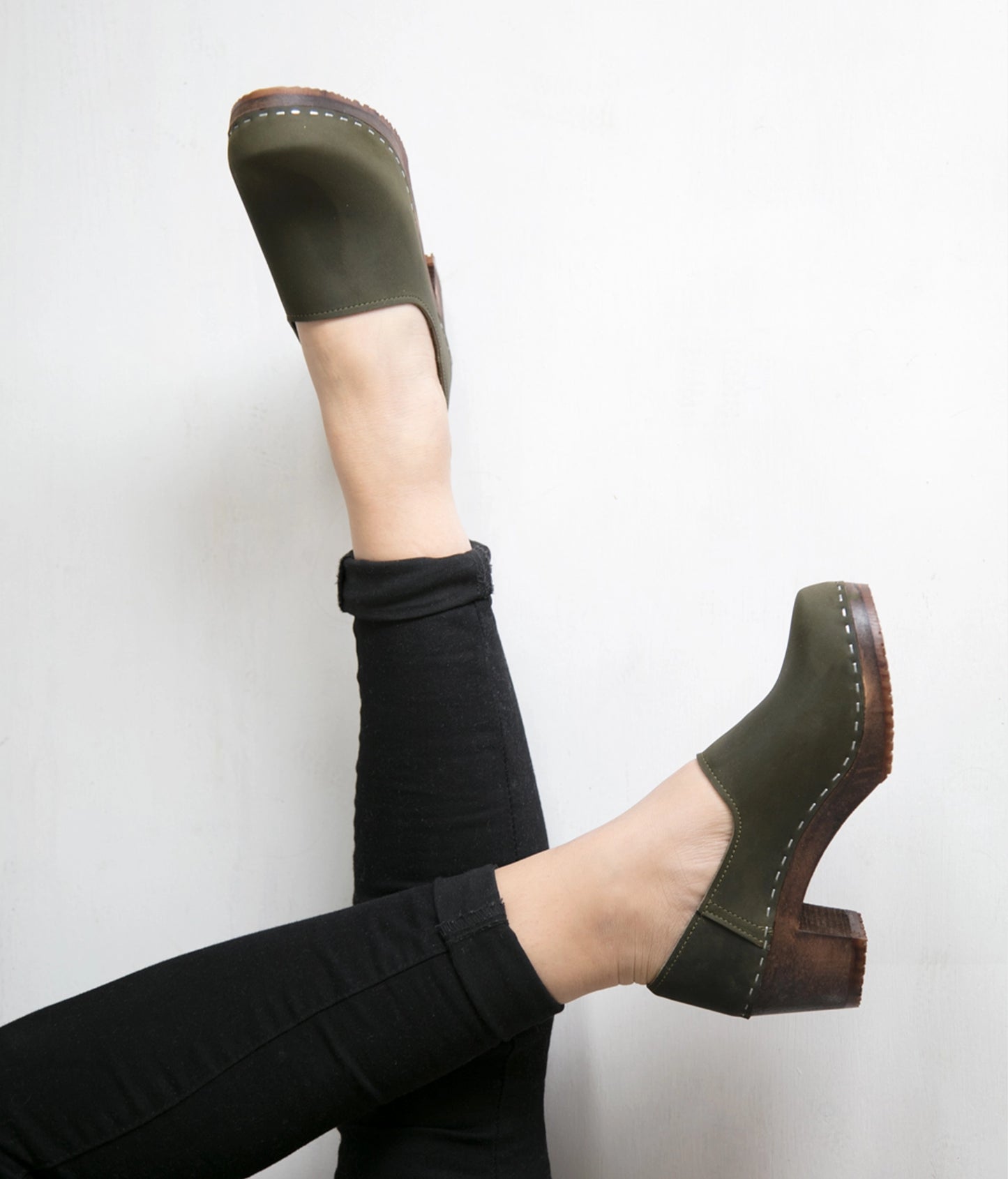 high heeled closed-back clogs in olive green nubuck leather stapled on a dark wooden base