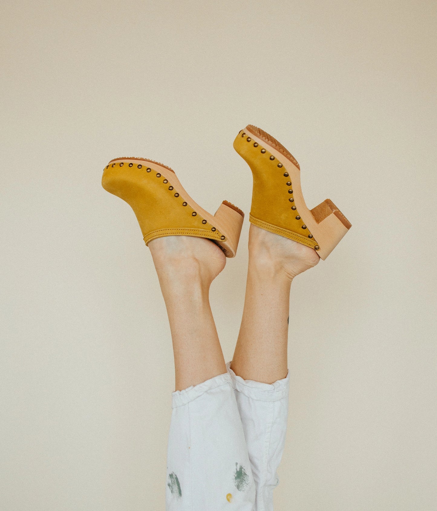 high heeled clog mules in yellow nubuck leather stapled on a light wooden base with brass gold studs