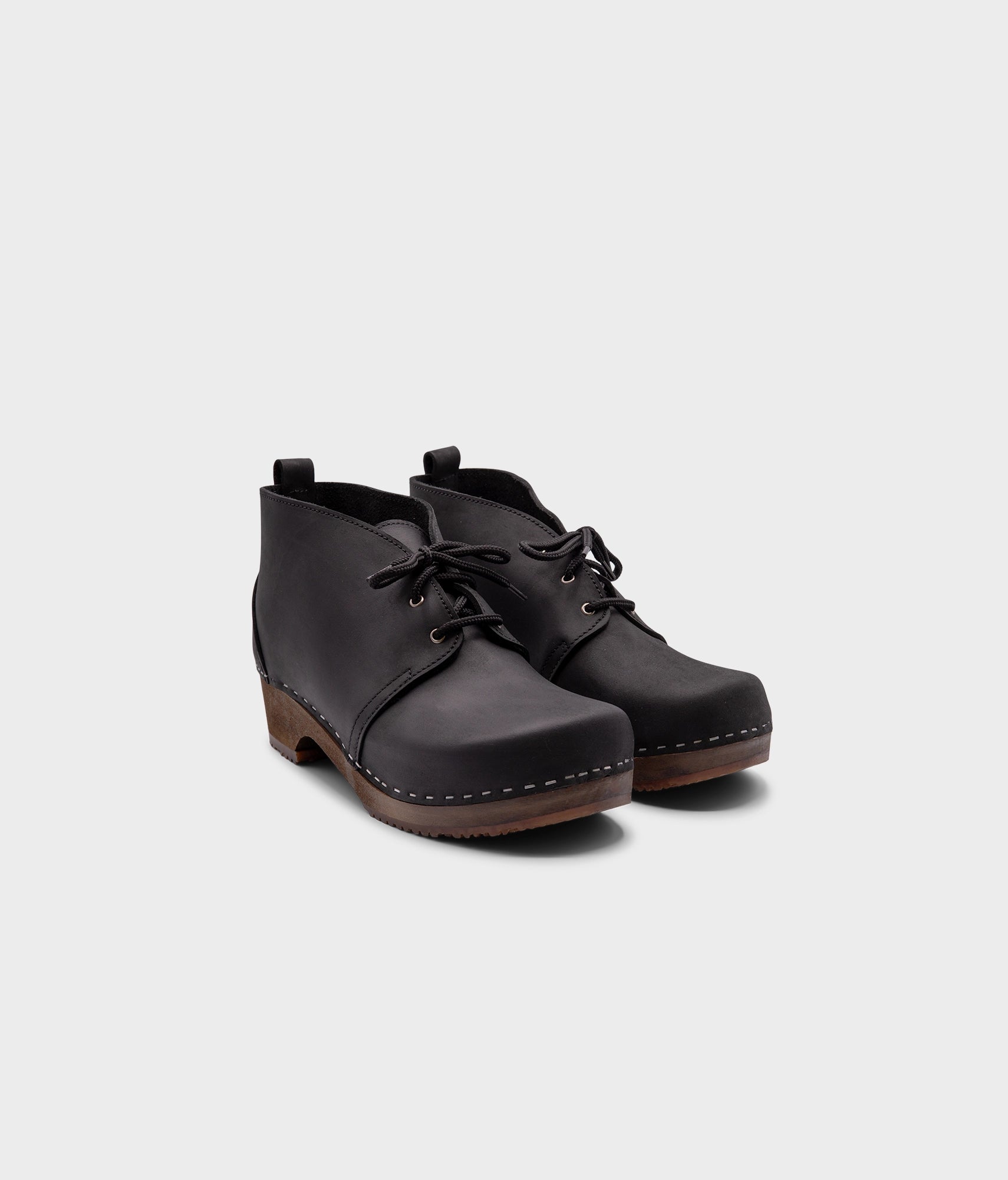 low heeled mens chukka clog boots in black nubuck leather stapled on a dark wooden base with black laces