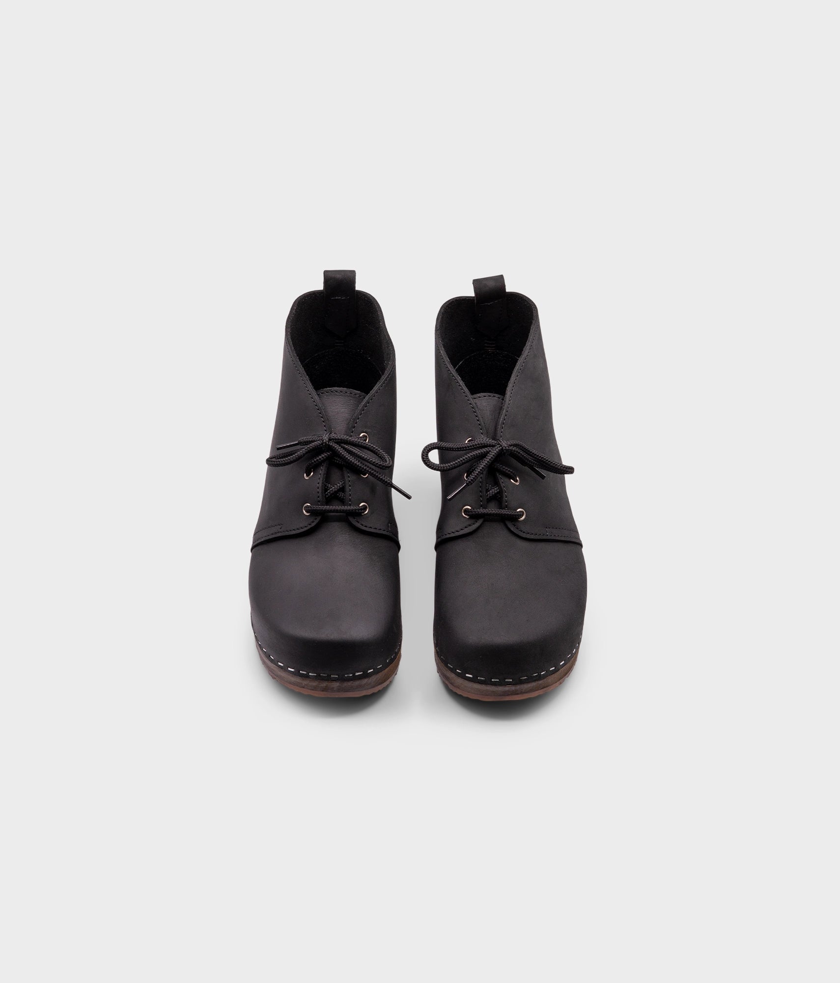 low heeled mens chukka clog boots in black nubuck leather stapled on a dark wooden base with black laces