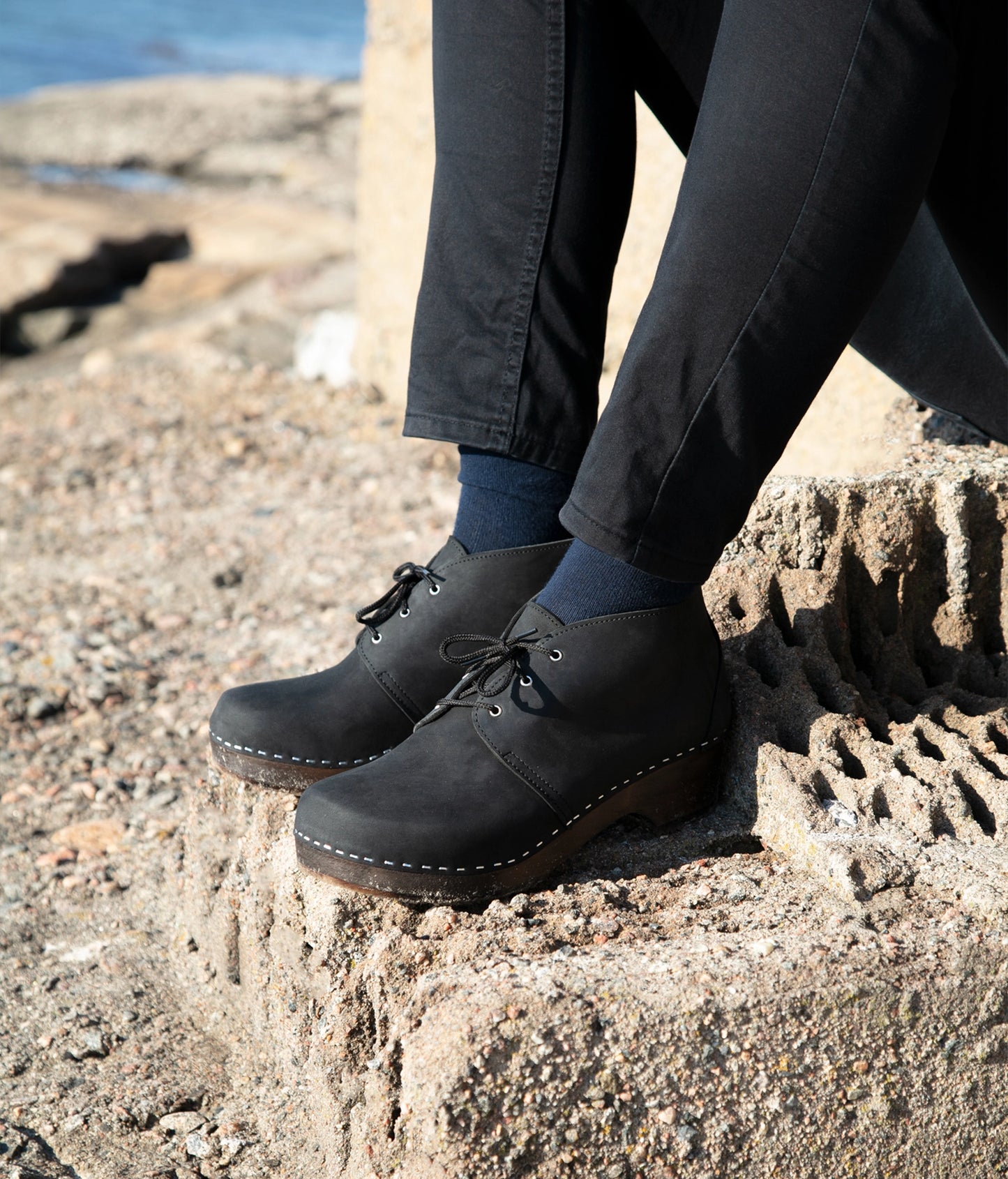 low heeled mens chukka clog boots in black nubuck leather stapled on a dark wooden base with black laces