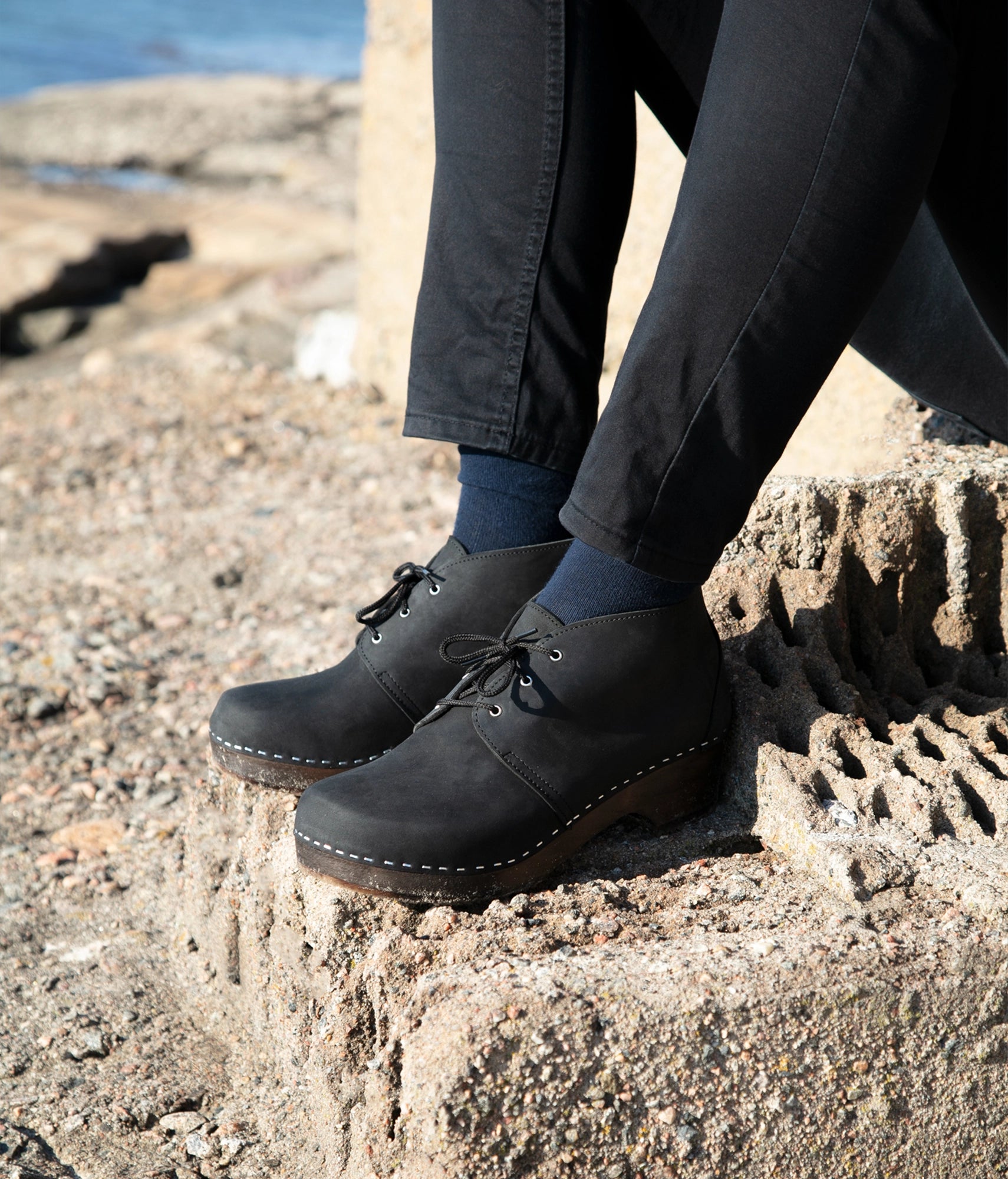 low heeled mens chukka clog boots in black nubuck leather stapled on a dark wooden base with black laces