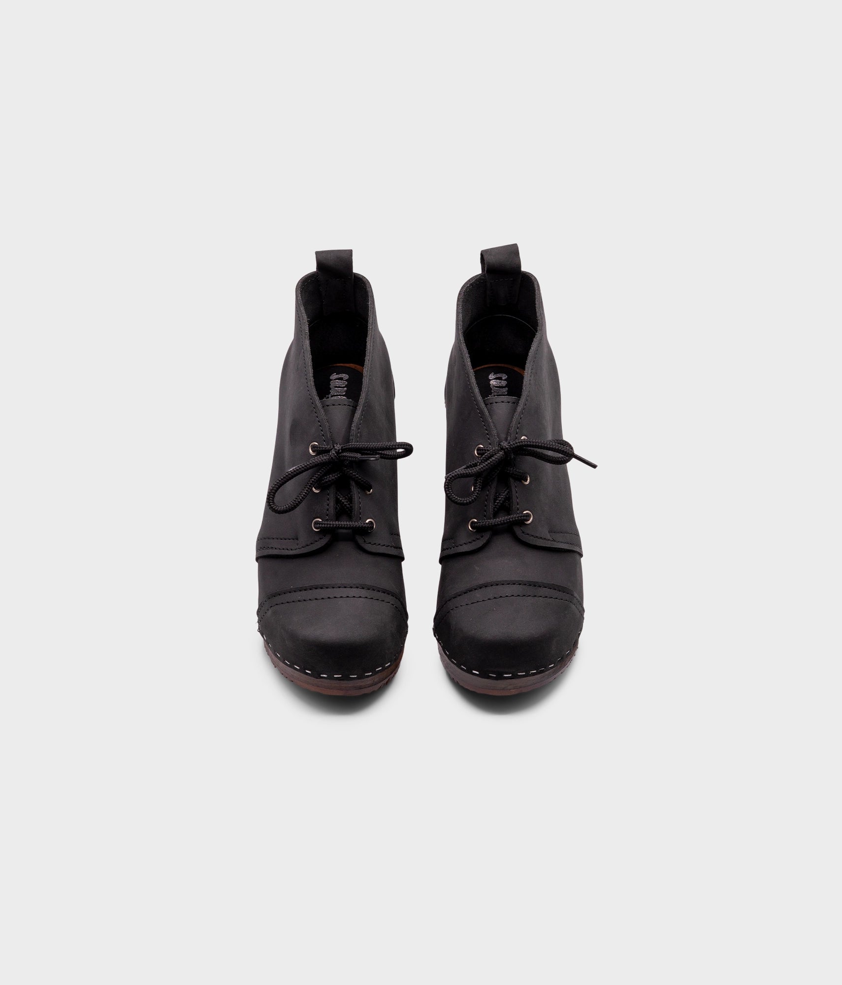 high heeled chukka clog boots in black nubuck leather stapled on a dark wooden base with black laces