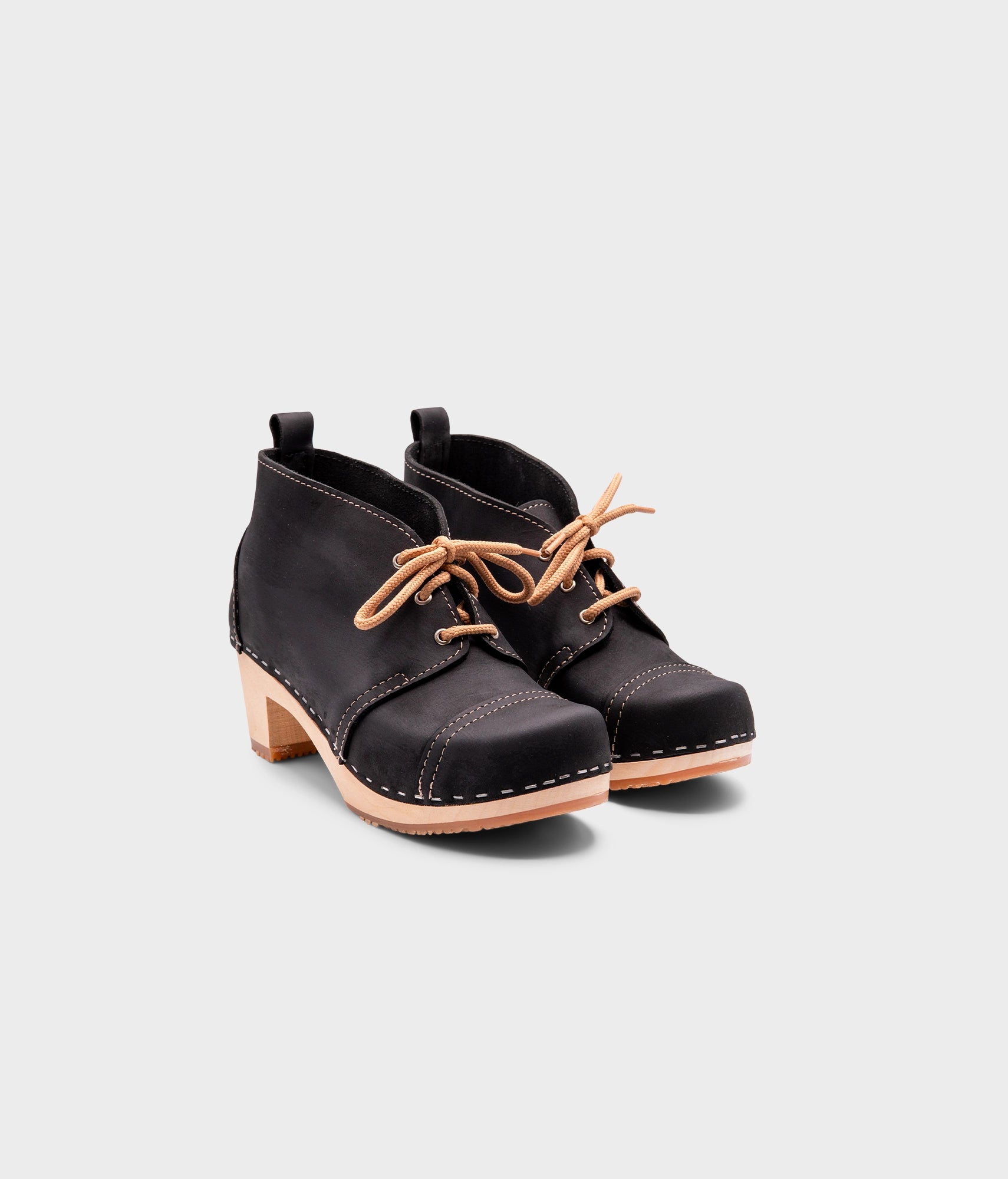 high heeled chukka clog boots in black nubuck leather stapled on a light wooden base with beige laces