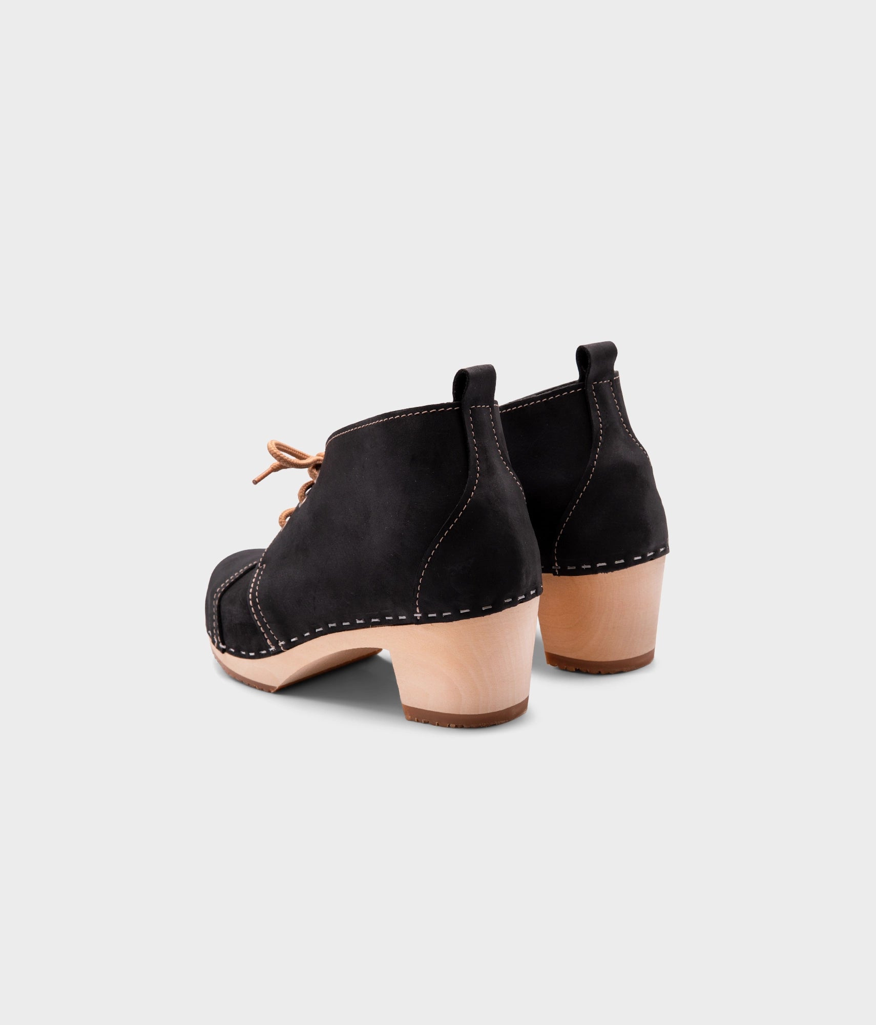 high heeled chukka clog boots in black nubuck leather stapled on a light wooden base with beige laces