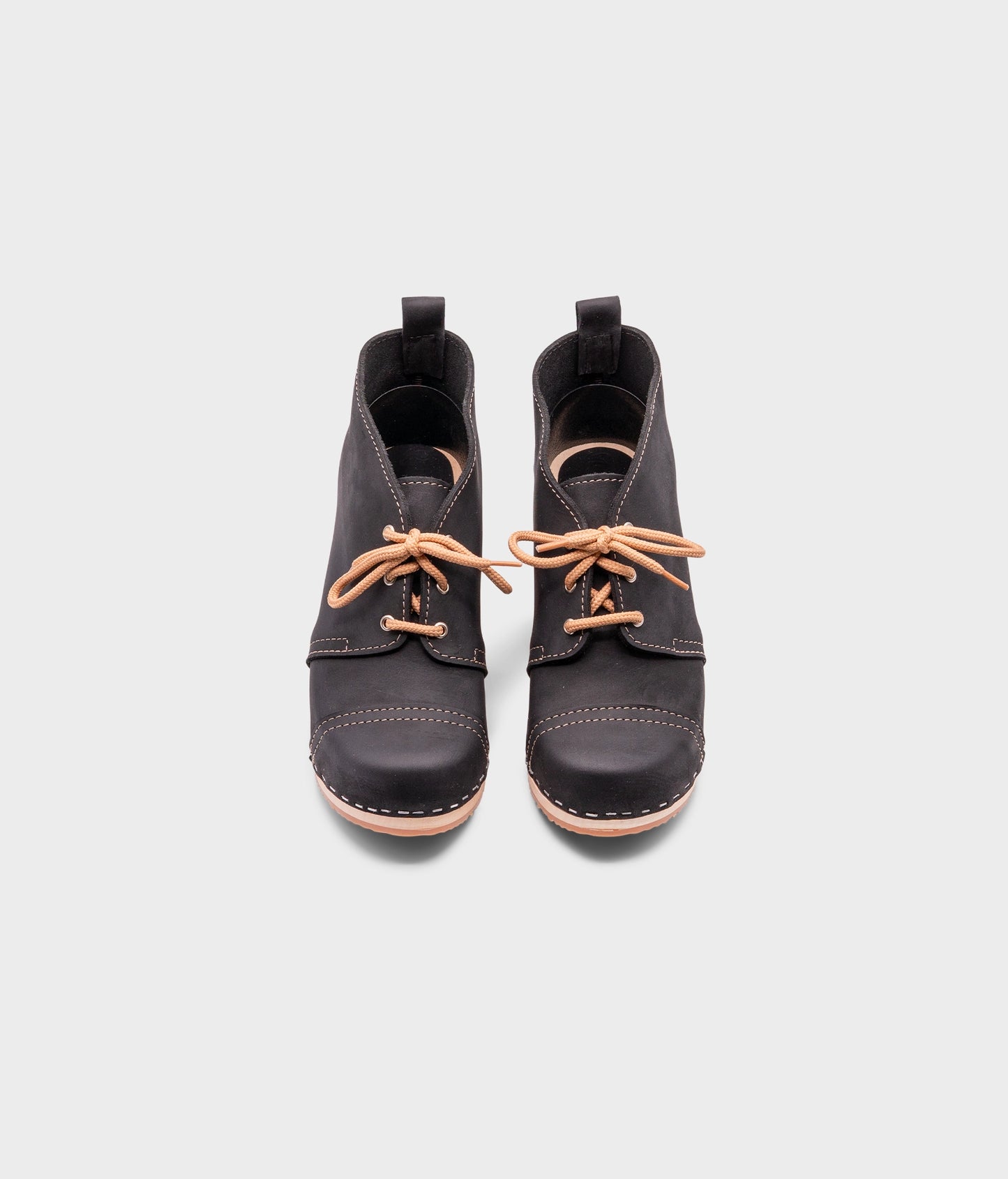 high heeled chukka clog boots in black nubuck leather stapled on a light wooden base with beige laces