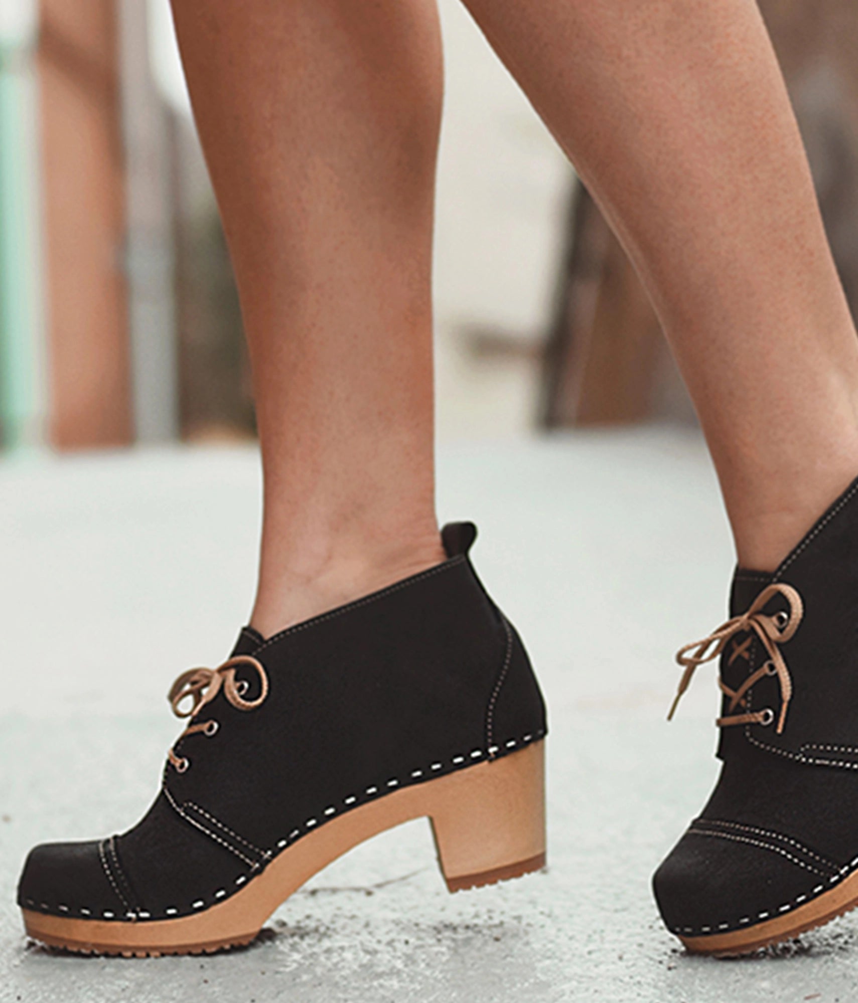 high heeled chukka clog boots in navy blue nubuck leather stapled on a dark wooden base with brown laces