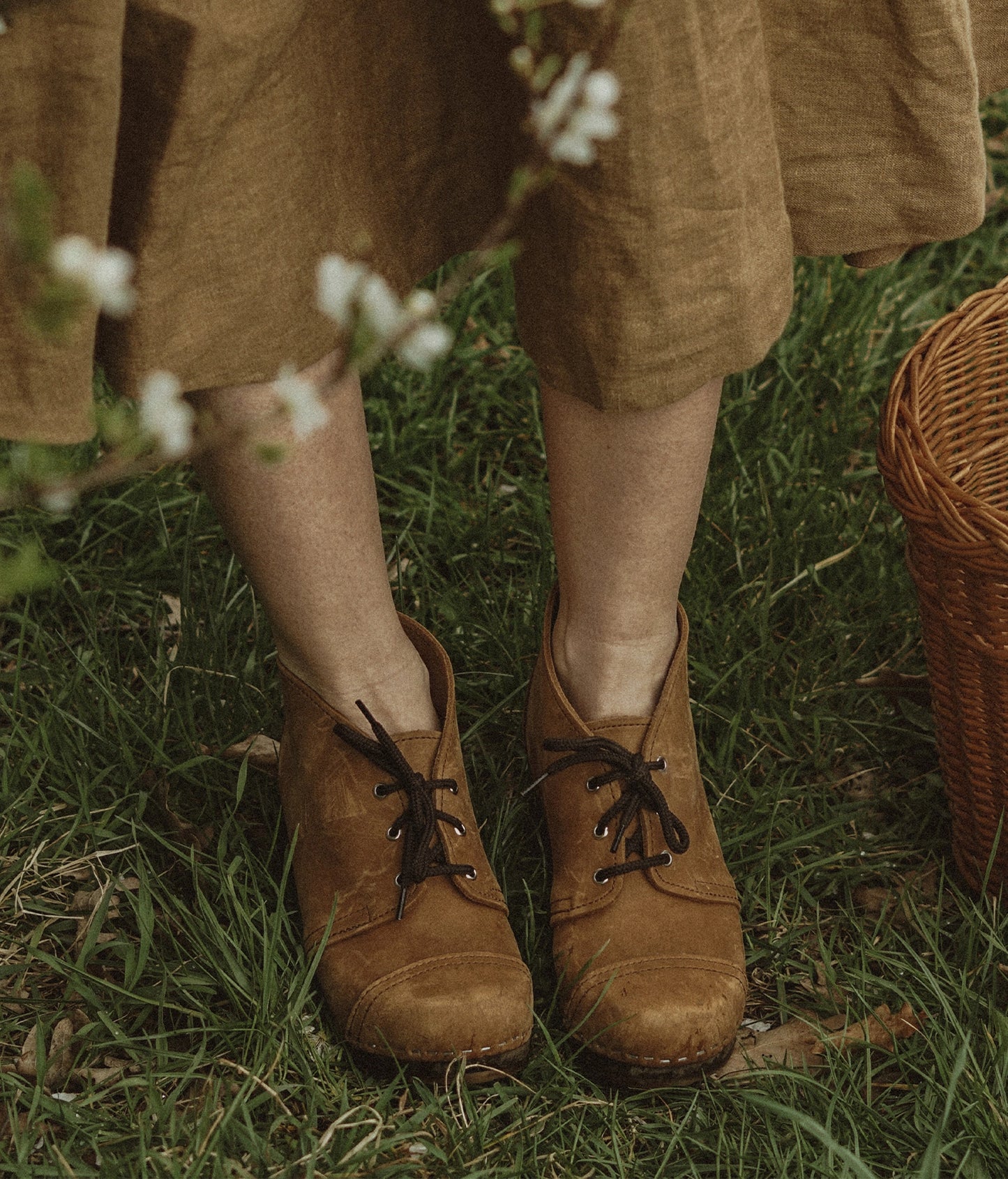 high heeled chukka clog boots in light brown nubuck leather stapled on a dark wooden base with brown laces