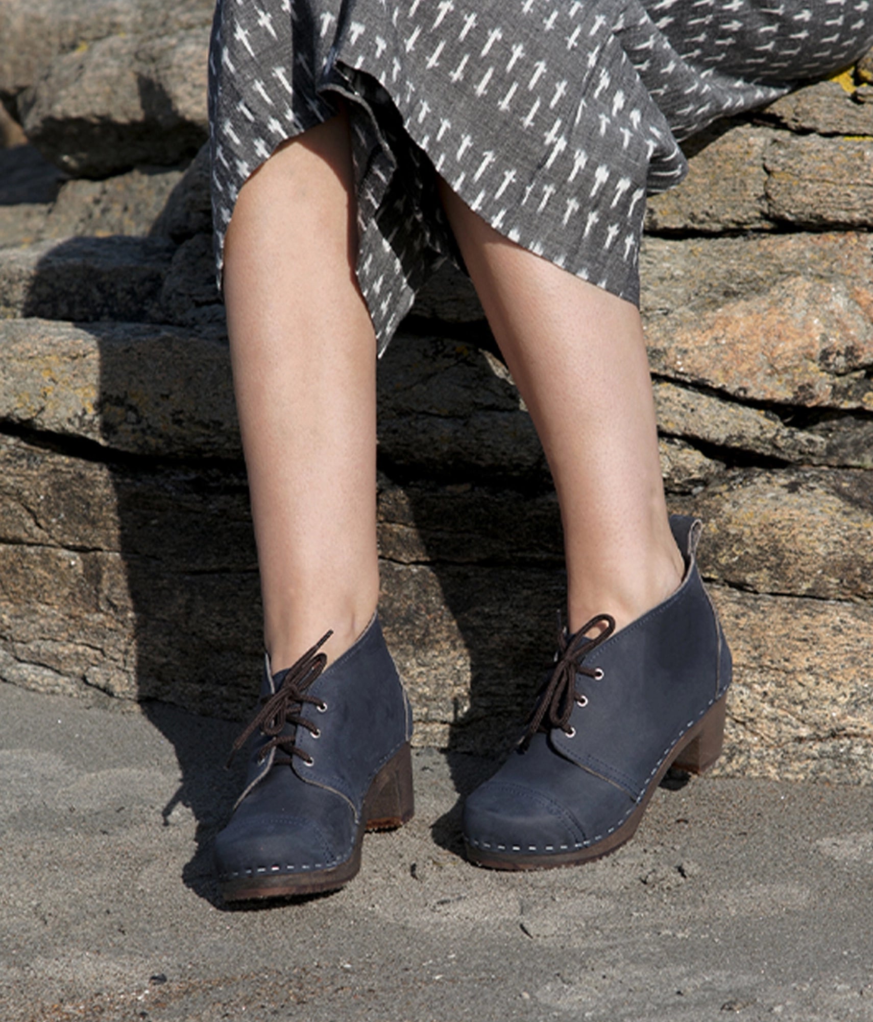 high heeled chukka clog boots in navy blue nubuck leather stapled on a dark wooden base with brown laces