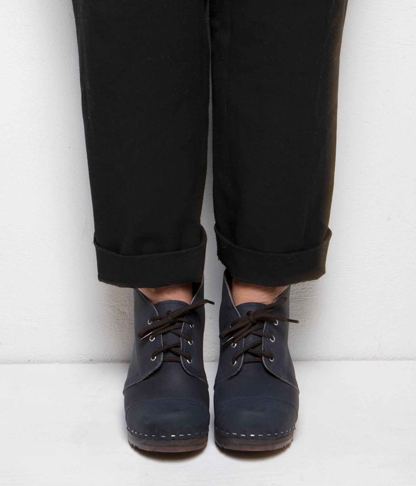 high heeled chukka clog boots in navy blue nubuck leather stapled on a dark wooden base with brown laces