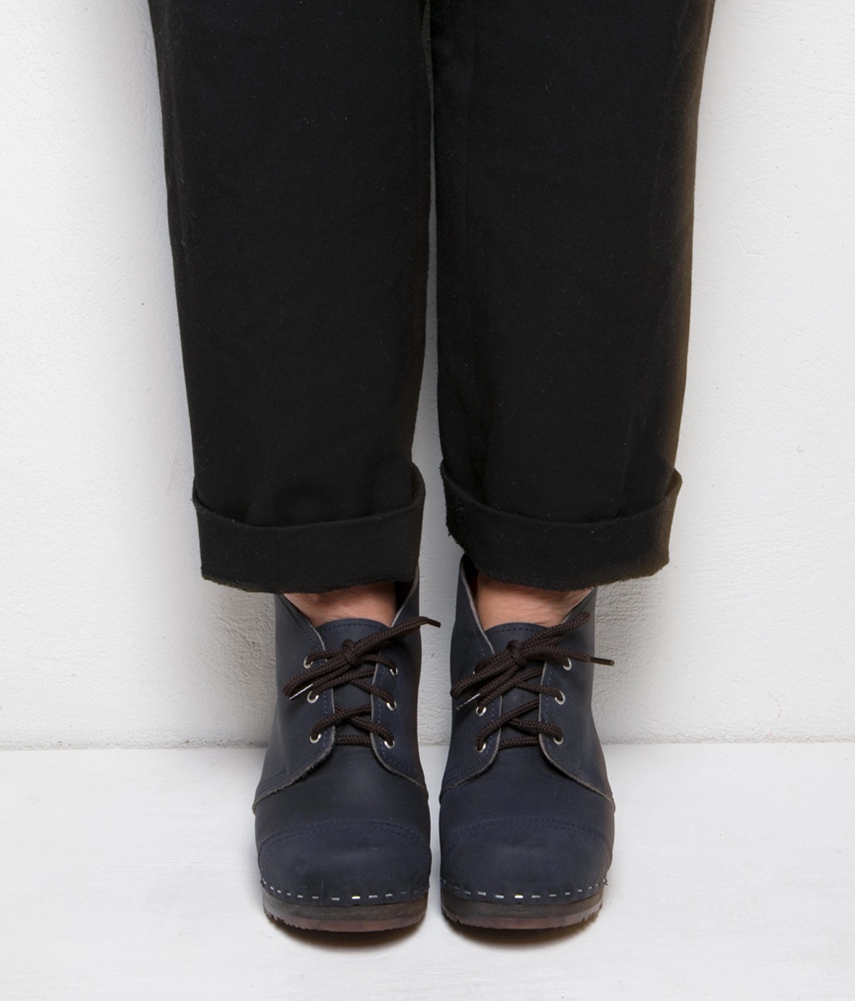 high heeled chukka clog boots in navy blue nubuck leather stapled on a dark wooden base with brown laces