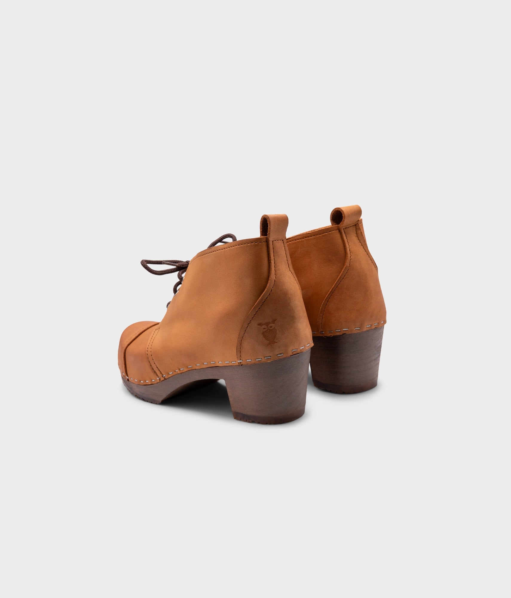 high heeled chukka clog boots in light brown nubuck leather stapled on a dark wooden base with brown laces