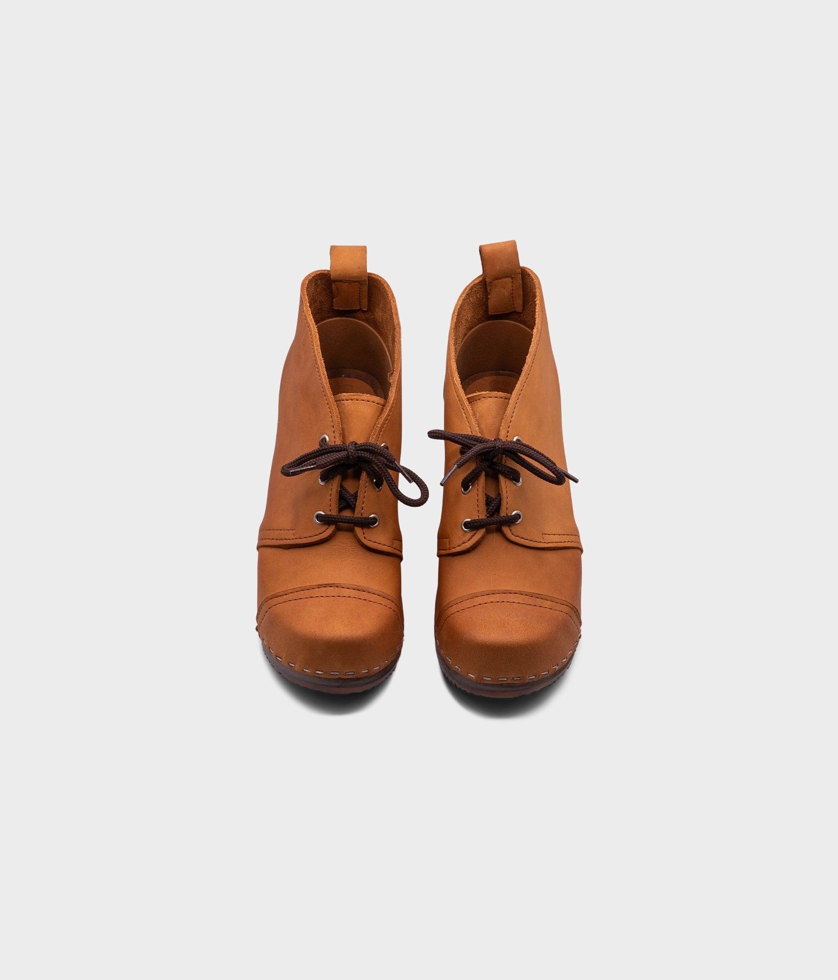 high heeled chukka clog boots in light brown nubuck leather stapled on a dark wooden base with brown laces