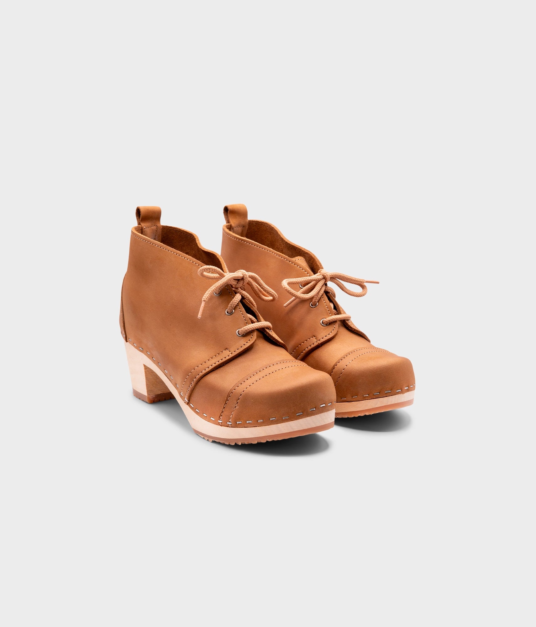 high heeled chukka clog boots in light brown nubuck leather stapled on a light wooden base with beige laces