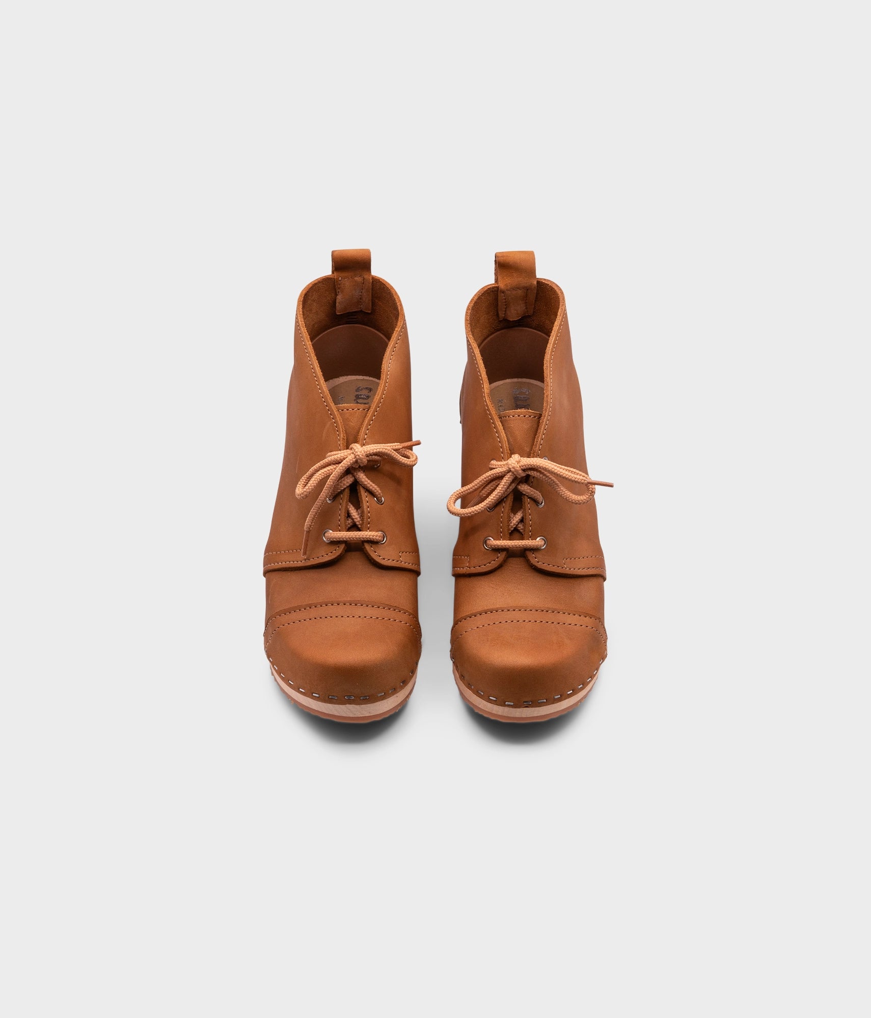high heeled chukka clog boots in light brown nubuck leather stapled on a light wooden base with beige laces