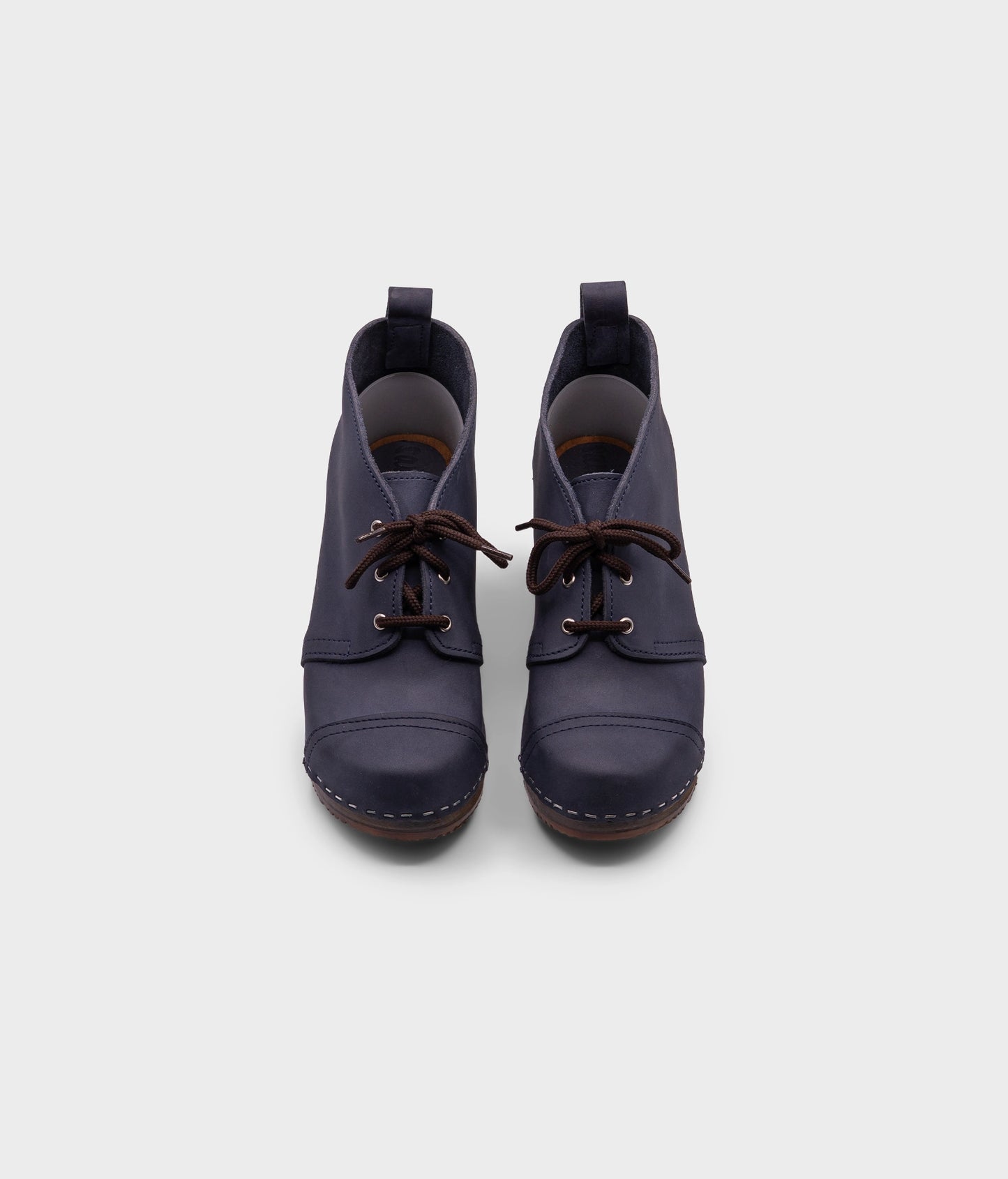 high heeled chukka clog boots in navy blue nubuck leather stapled on a dark wooden base with brown laces