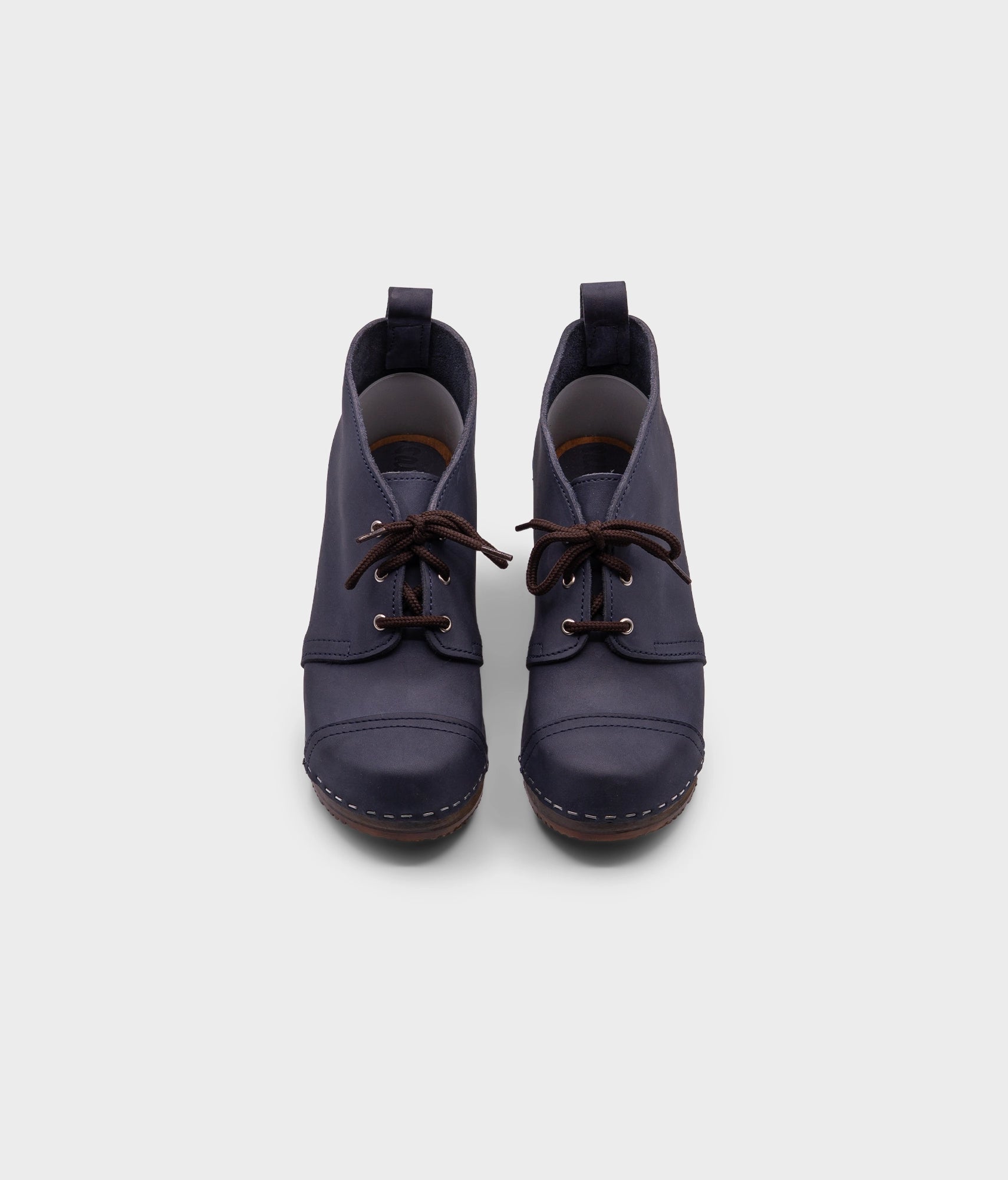 high heeled chukka clog boots in navy blue nubuck leather stapled on a dark wooden base with brown laces