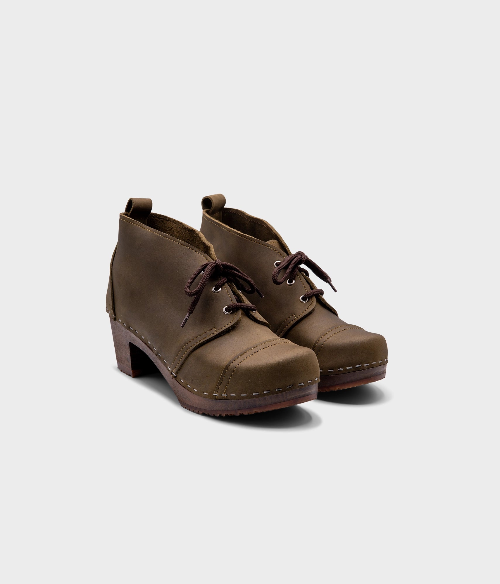 high heeled chukka clog boots in olive green nubuck leather stapled on a dark wooden base with brown laces
