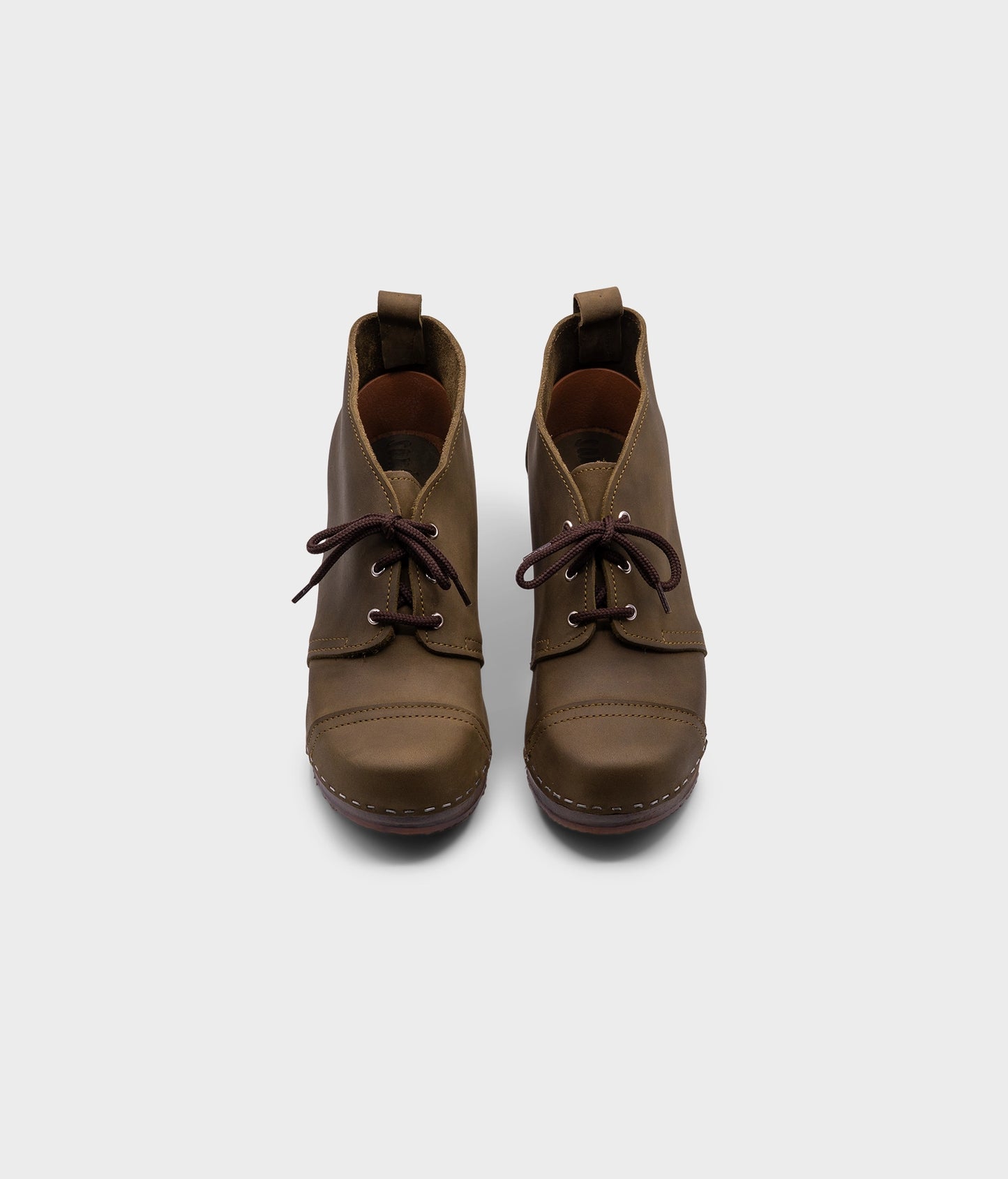 high heeled chukka clog boots in olive green nubuck leather stapled on a dark wooden base with brown laces